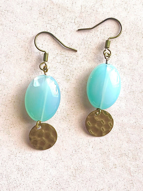 Aqua glass and yellow brass fish hook earrings on a pink backdrop