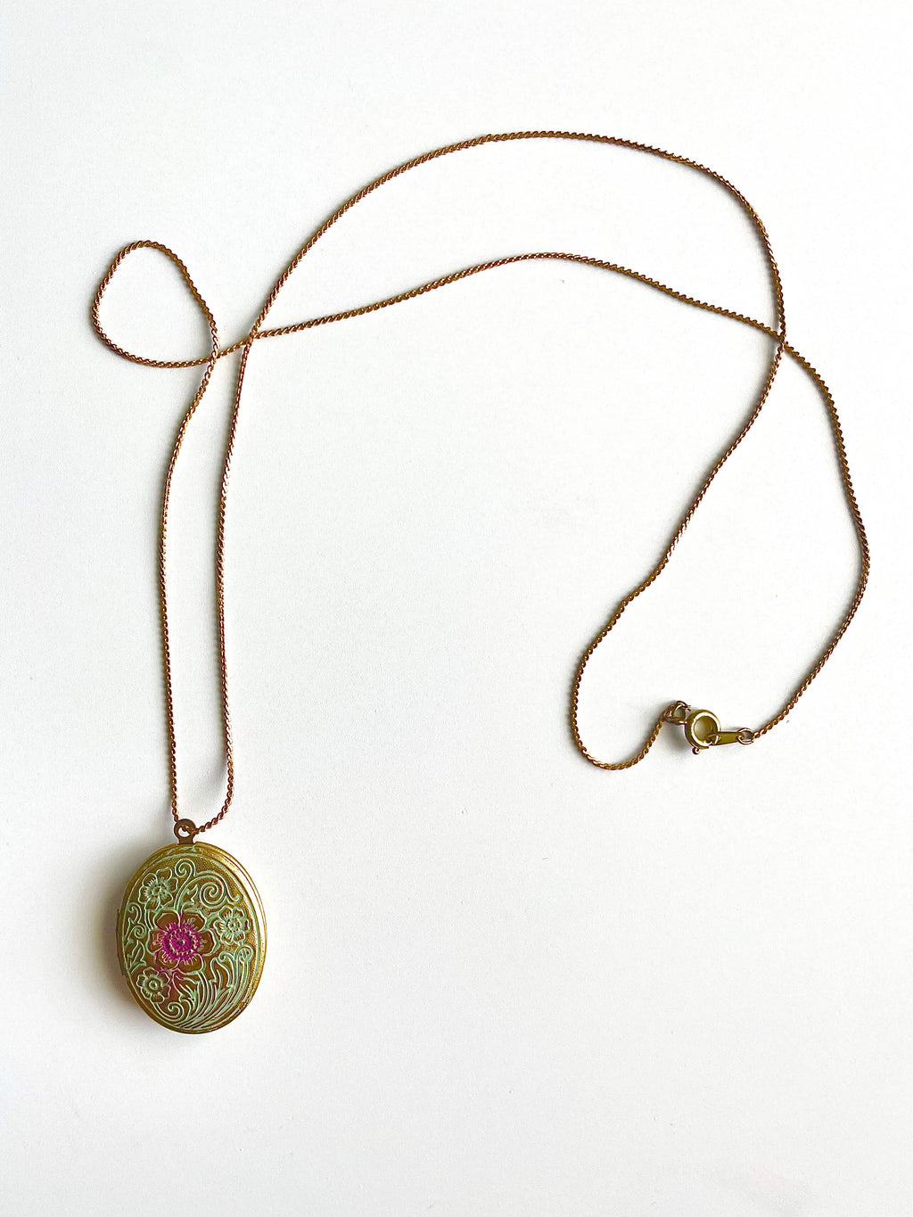 Yellow brass locket necklace with blue and purple patina on a white background