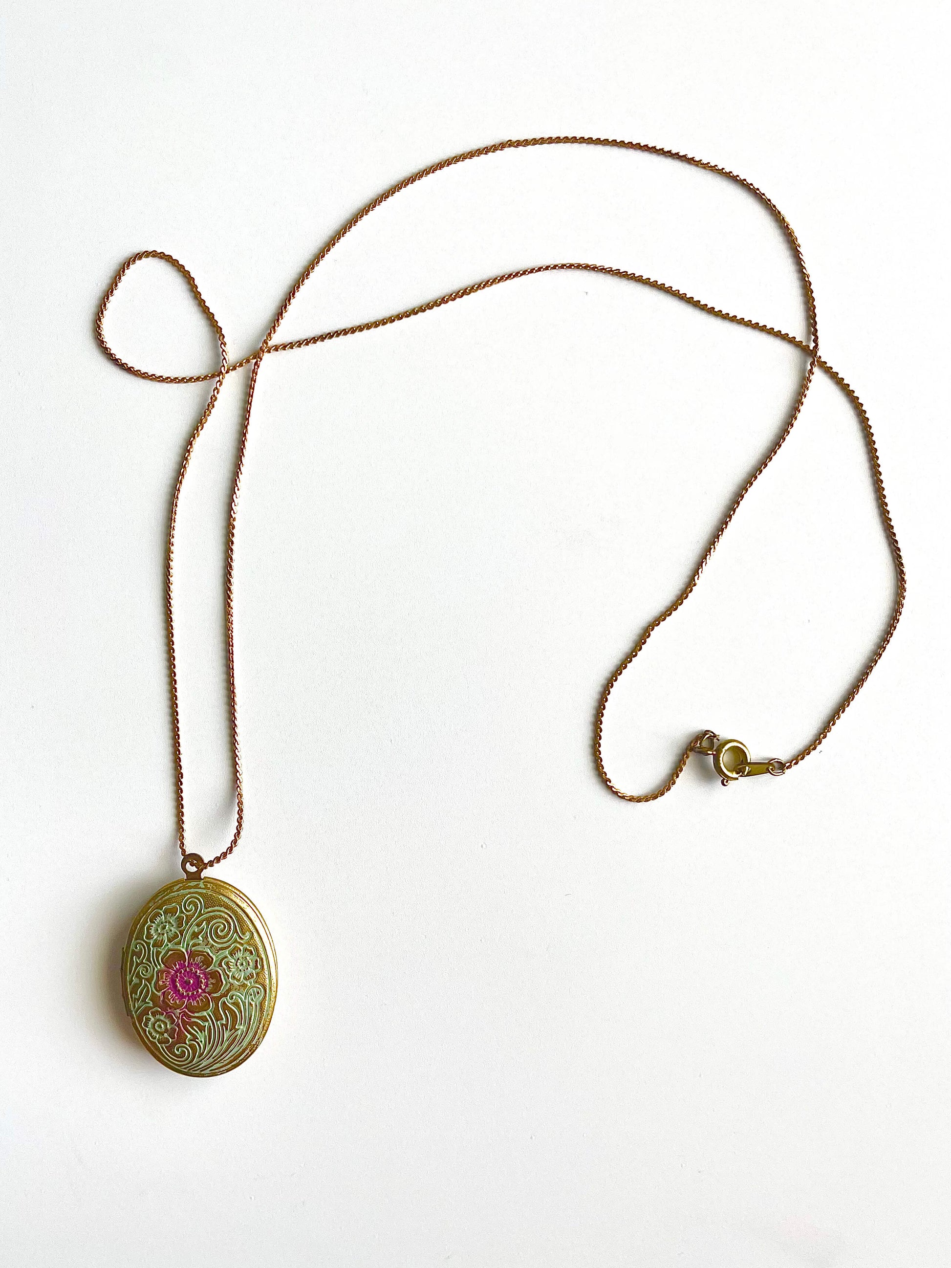 Yellow brass locket necklace with blue and purple patina on a white background