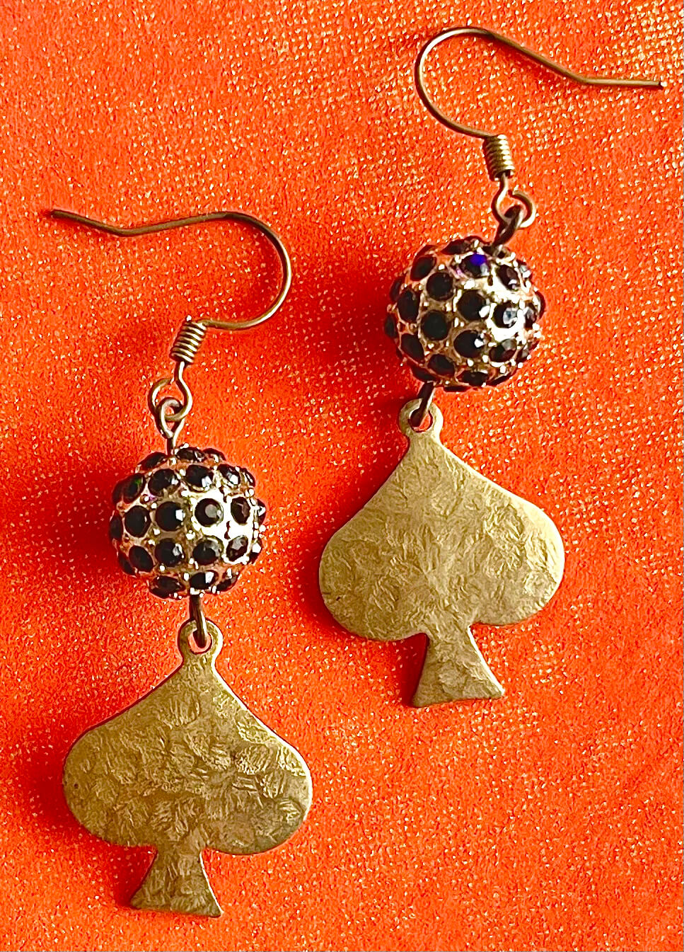 Yellow brass earrings with black crystal bead and hanging textured spade pendant on orange background