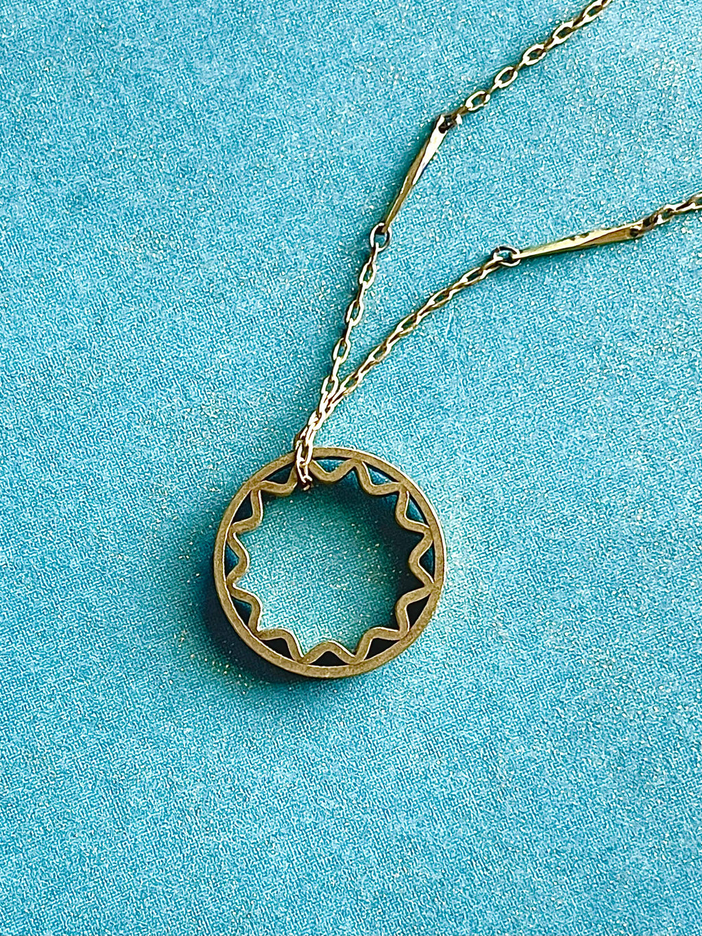 Yellow brass sun pendant on a yellow brass bar chain with a blue background
