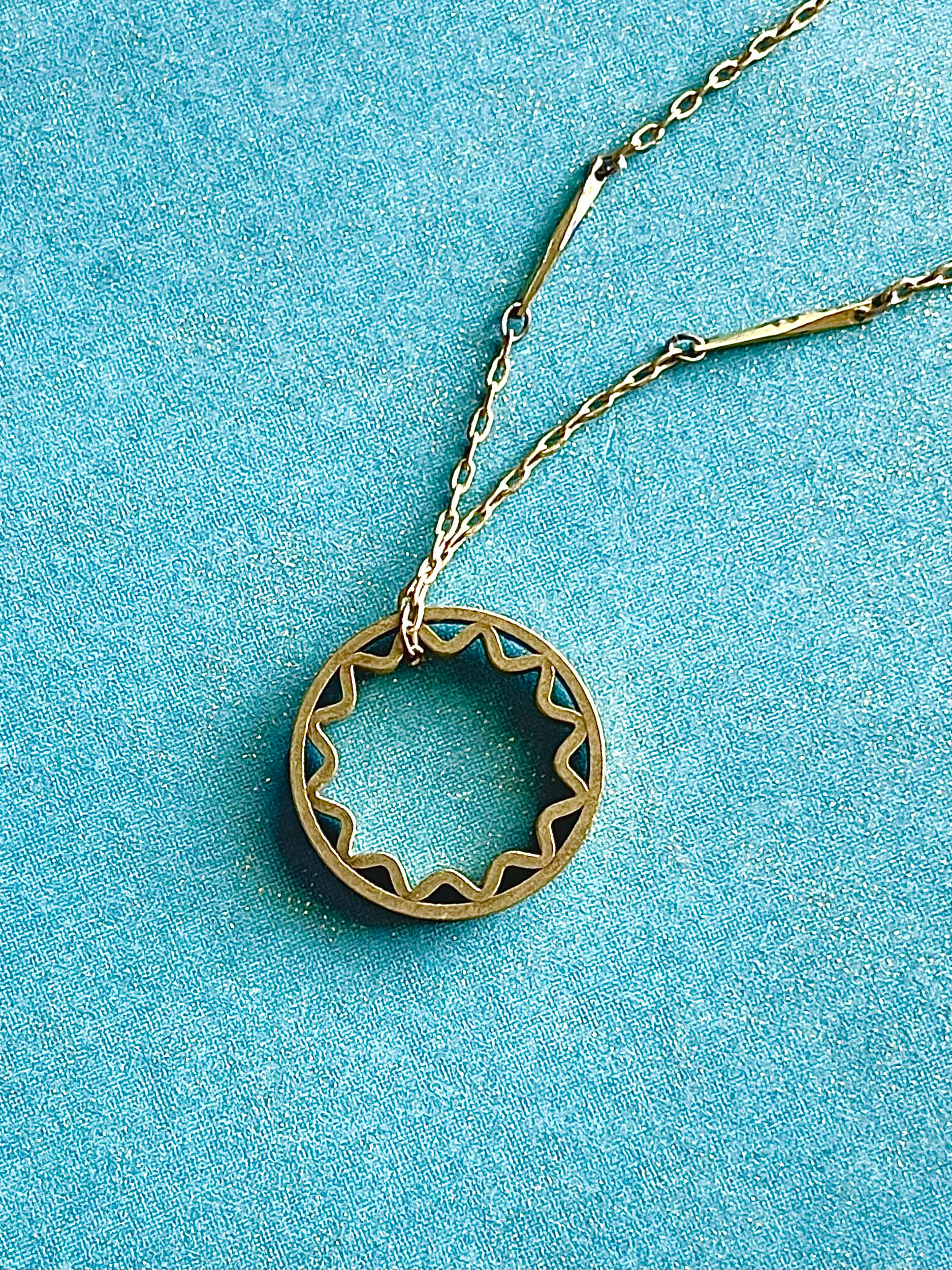 Yellow brass sun pendant on a yellow brass bar chain with a blue background