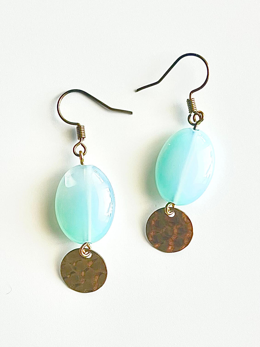 Aqua glass and yellow brass fish hook earrings on a pink backdrop