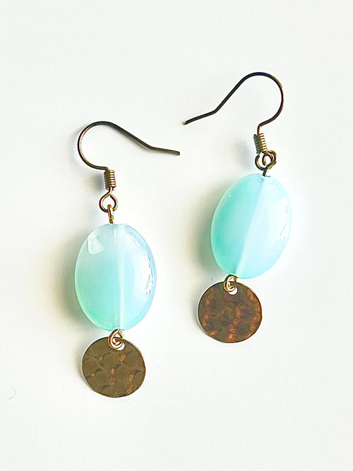 Aqua glass and yellow brass fish hook earrings on a pink backdrop