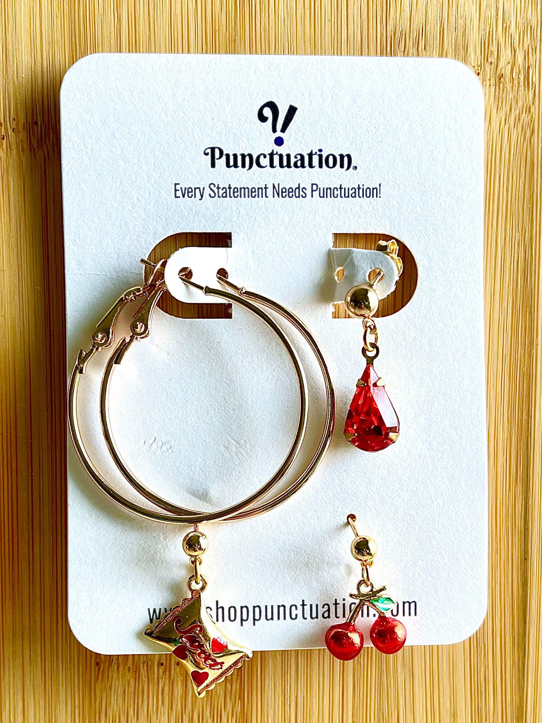 Yellow brass earring set with vintage hoops, red glass crystal dangle earring, candy wrapper charm dangle earring, and red and green enamel cherry charm dangle earring 