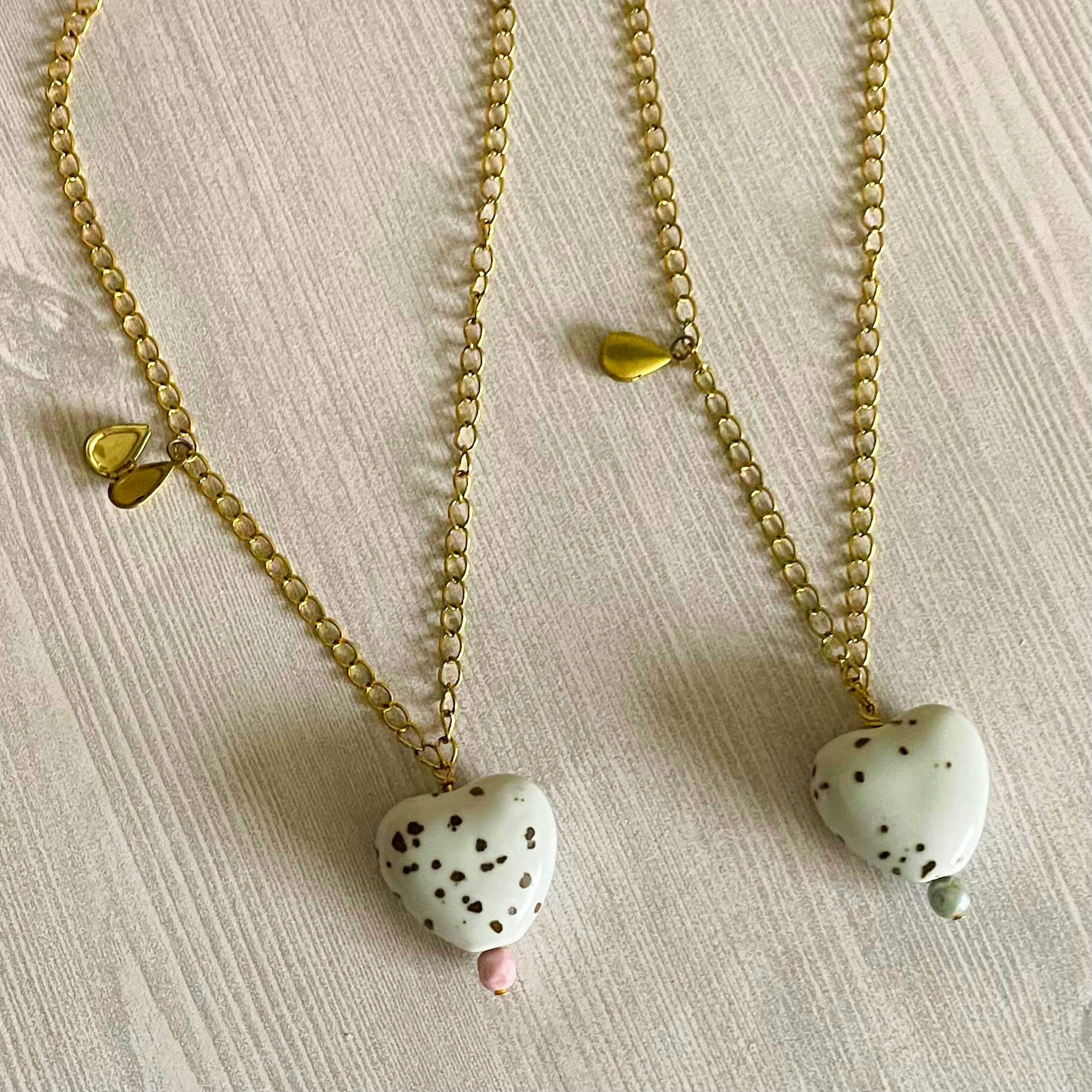 Two yellow brass necklaces with white and brown ceramic heart pendants and teardrop locket charms. 