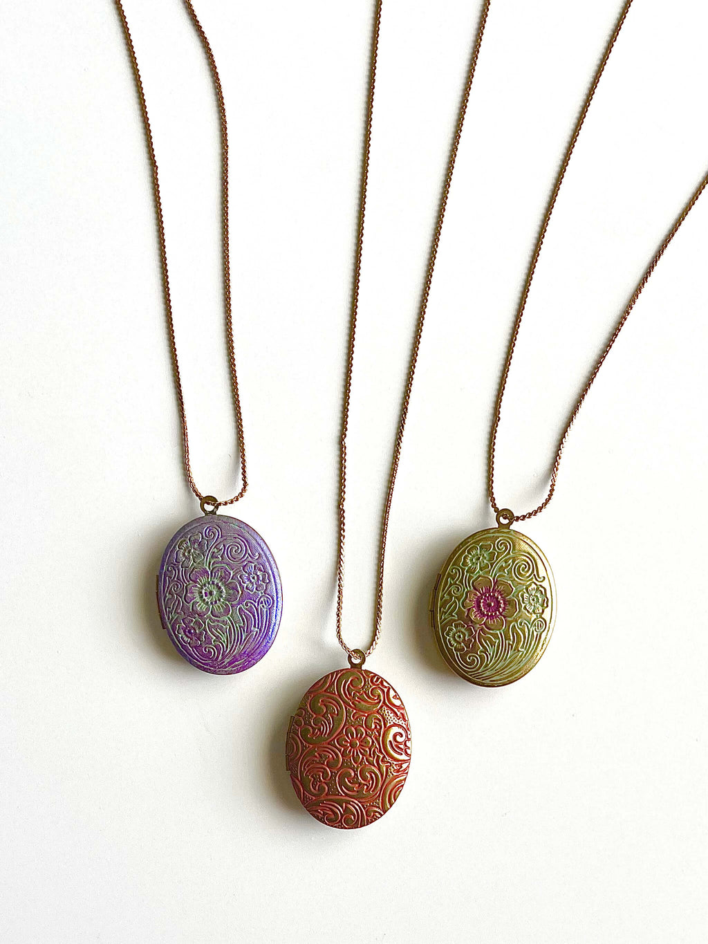 Multiple colored patina locket necklaces on a shite background