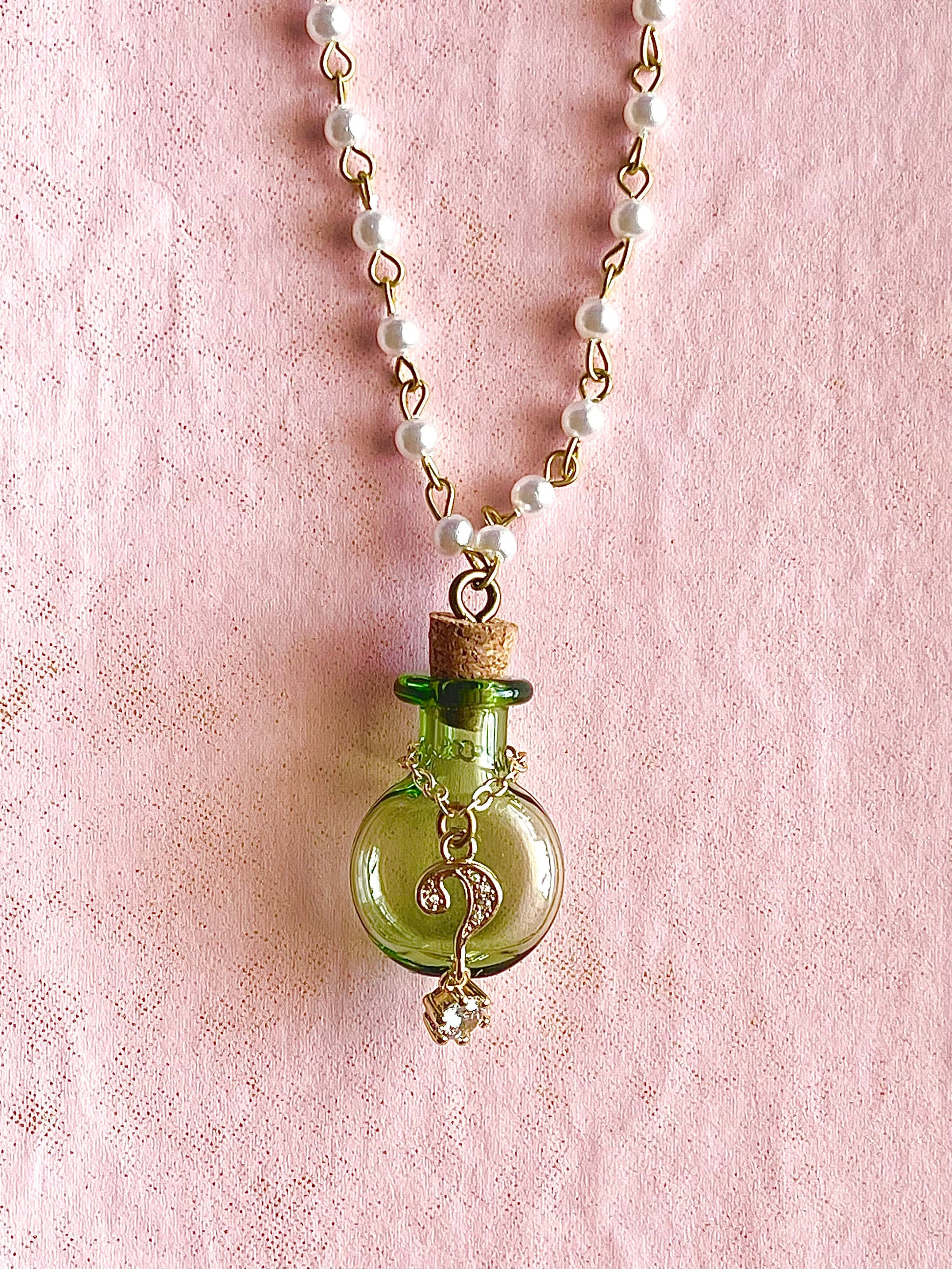 White faux pearl chain with green bottle and gold question mark pendant necklace on pink background