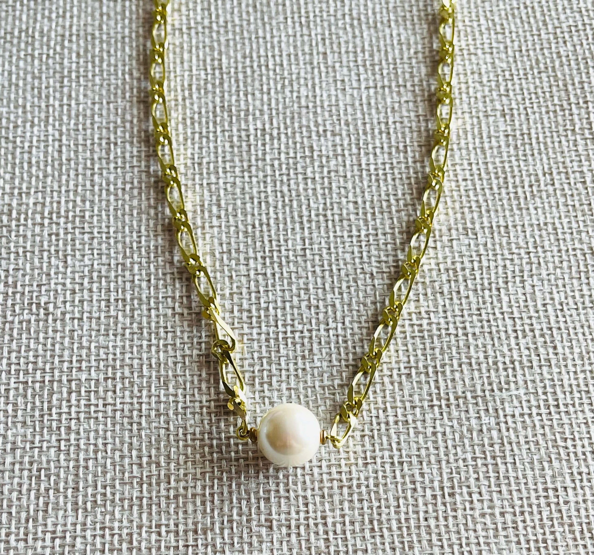 Yellow brass chain necklace with white glass Pearl on tan background