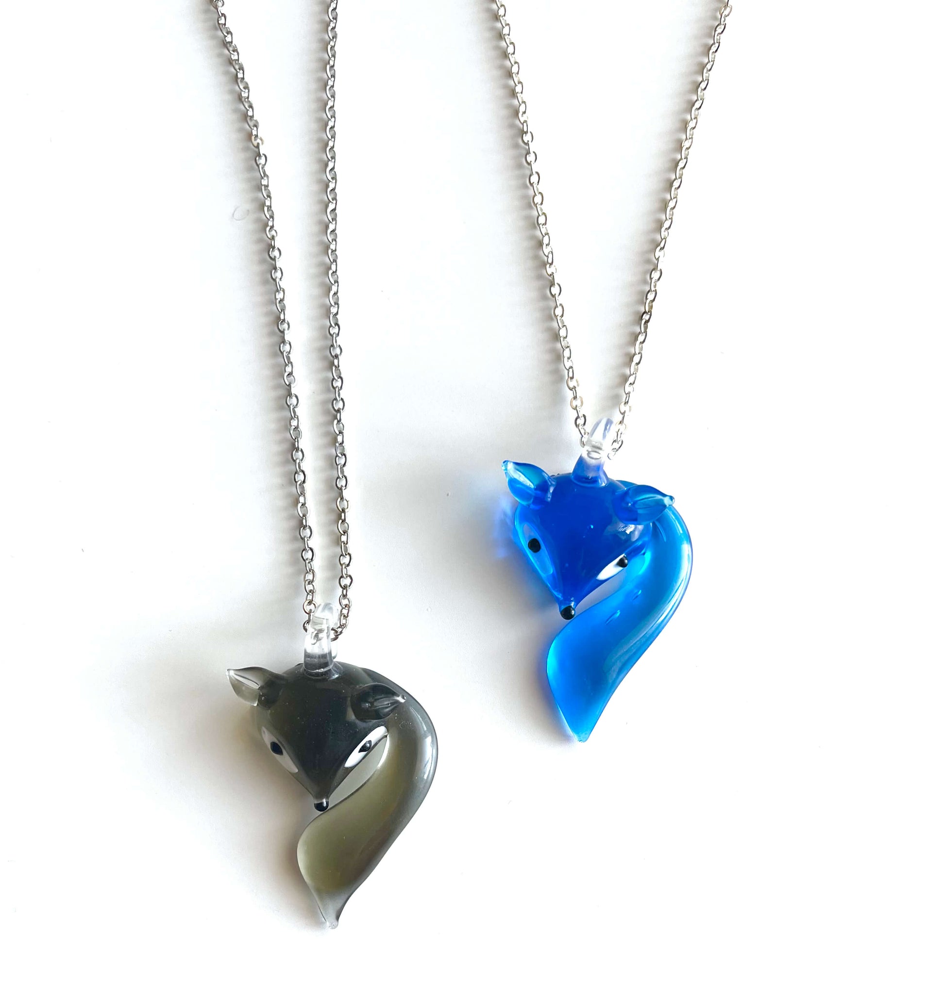 Two fox pendants, one blue and one gray, on silver chains against a white background.