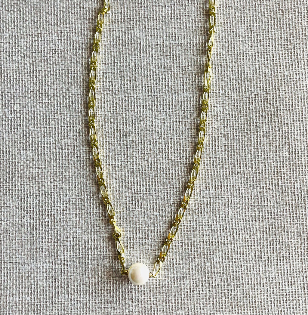 Yellow brass chain necklace with white pearl on tan background