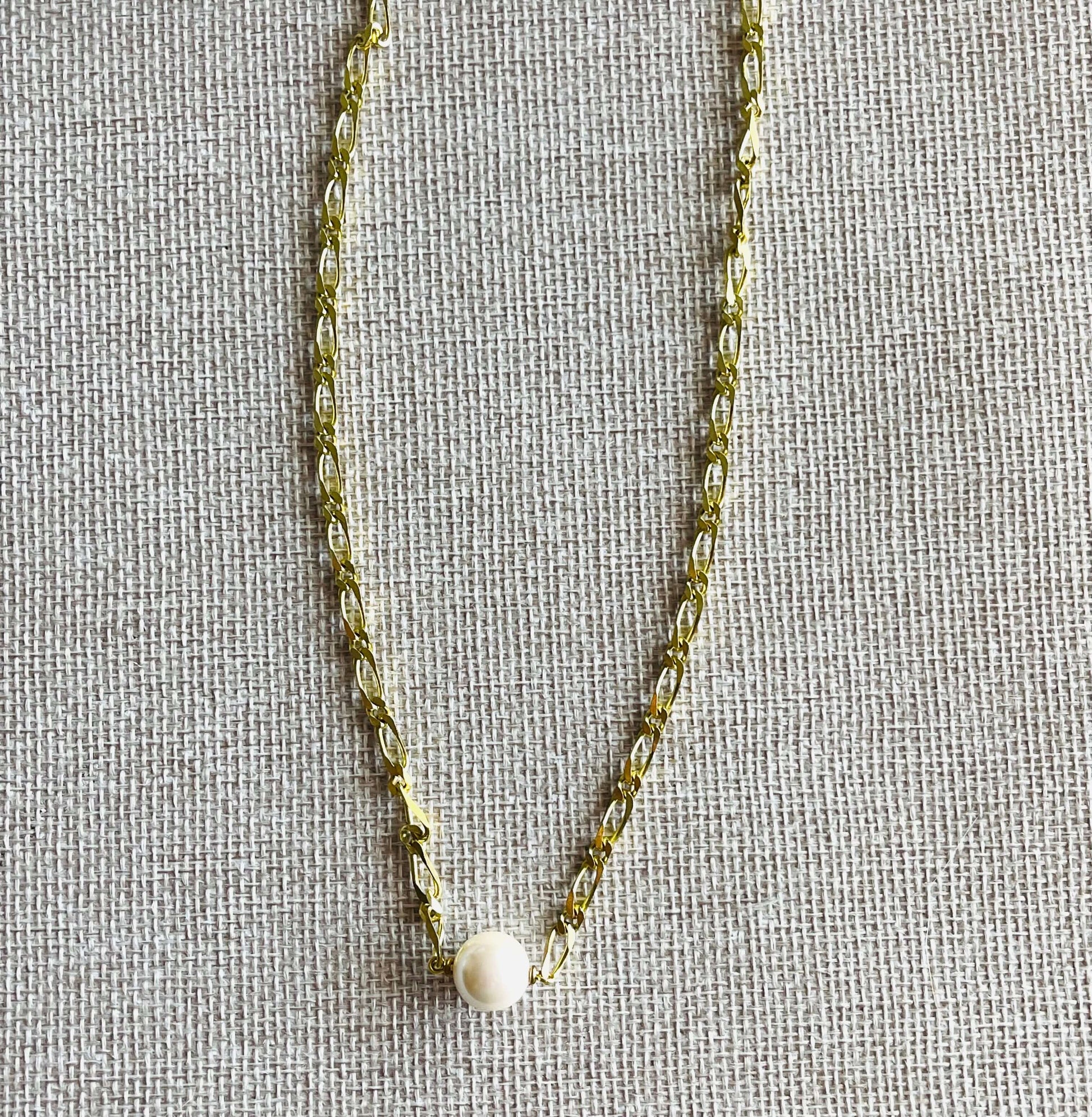 Yellow brass chain necklace with white pearl on tan background