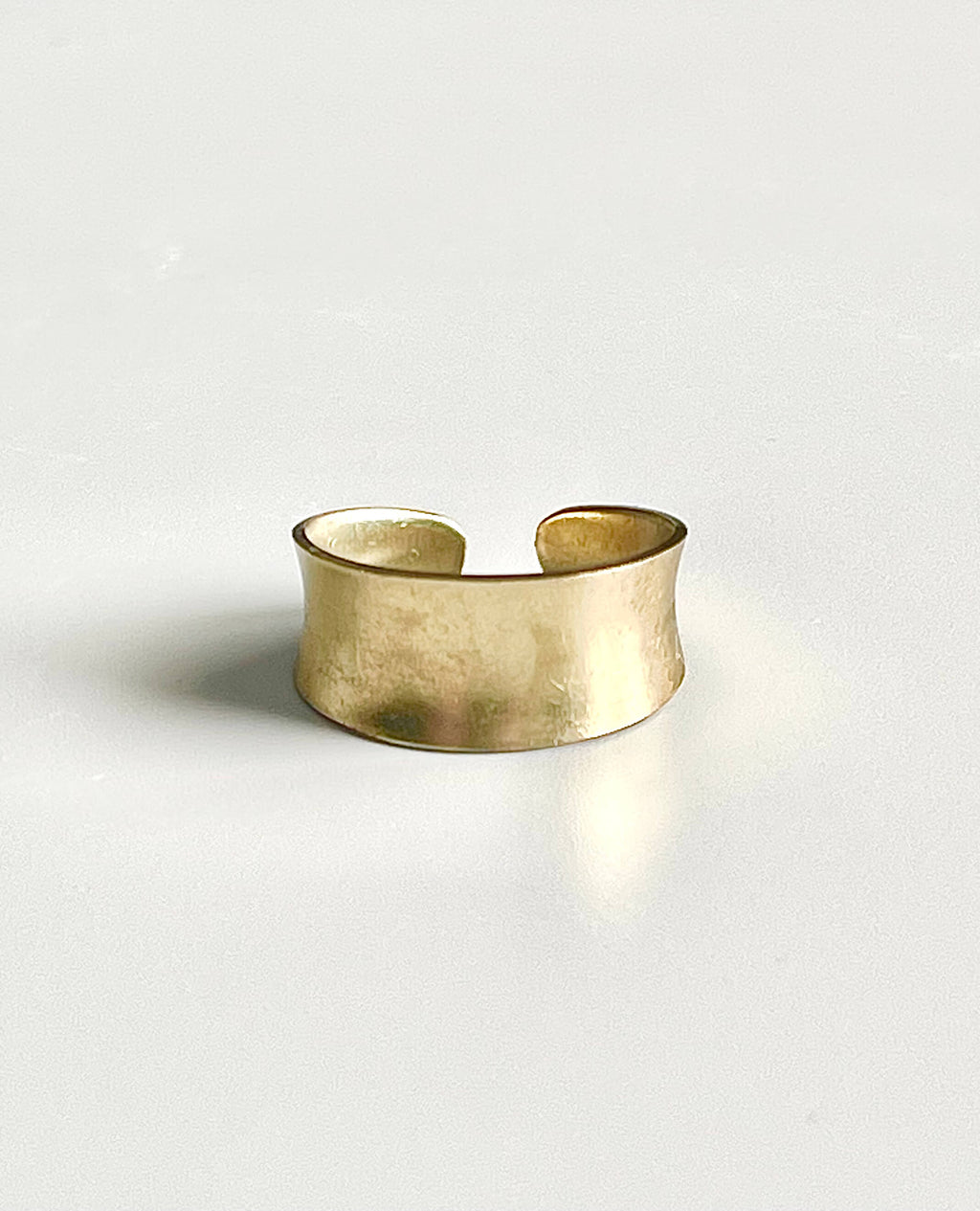 Yellow brass narrow adjustable concave ring on a white backdrop