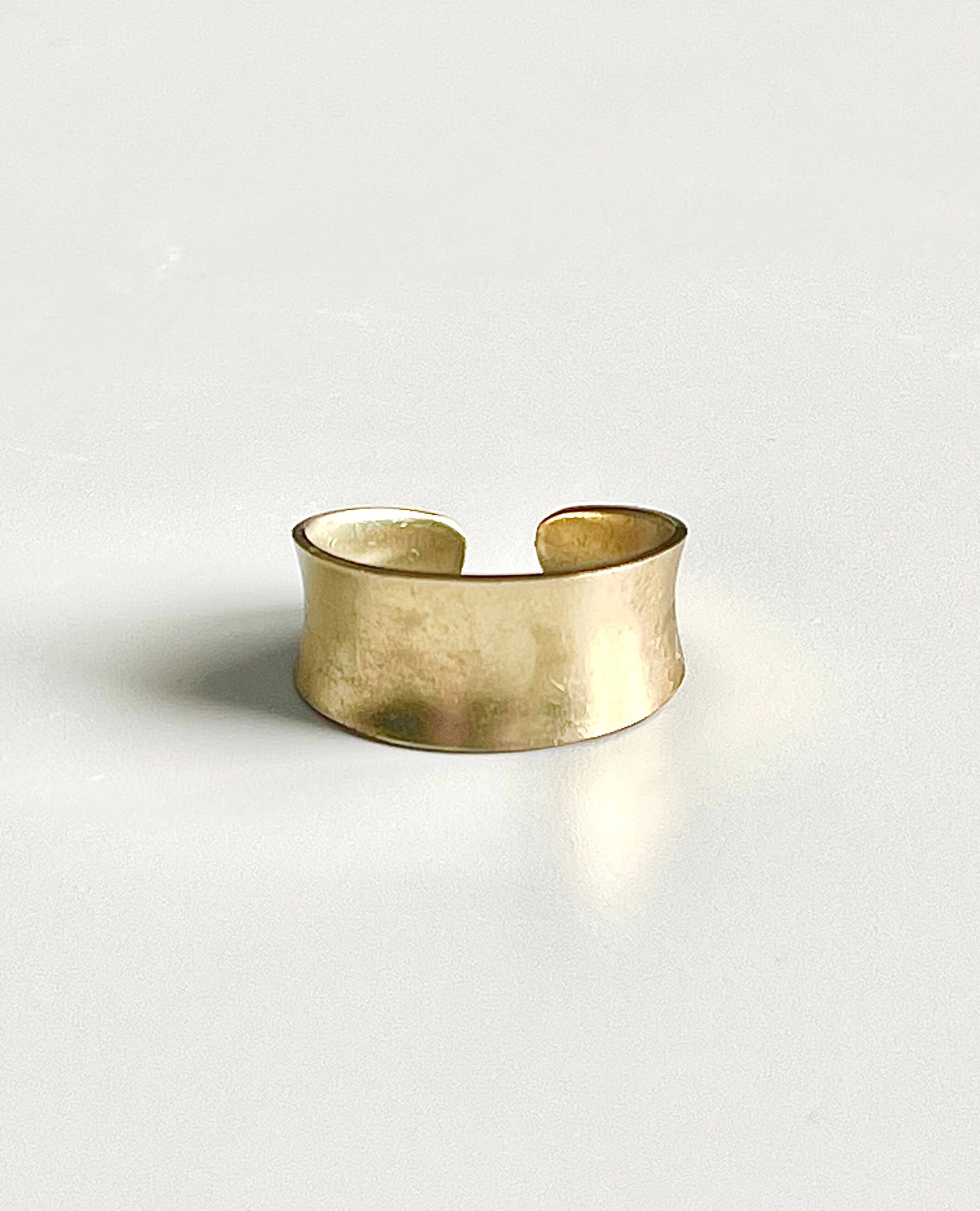 Yellow brass narrow adjustable concave ring on a white backdrop
