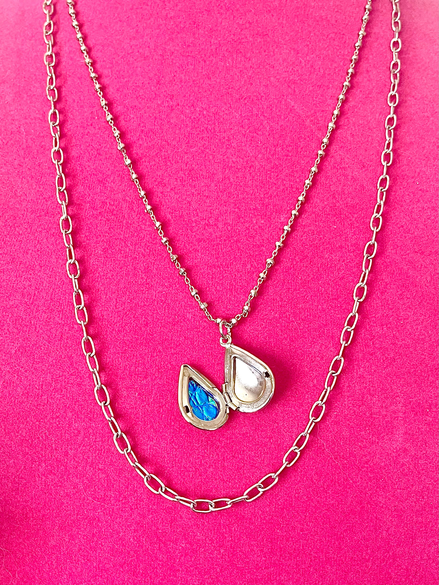 Silver chains with an open teardrop shaped locket and blue lining on a pink background
