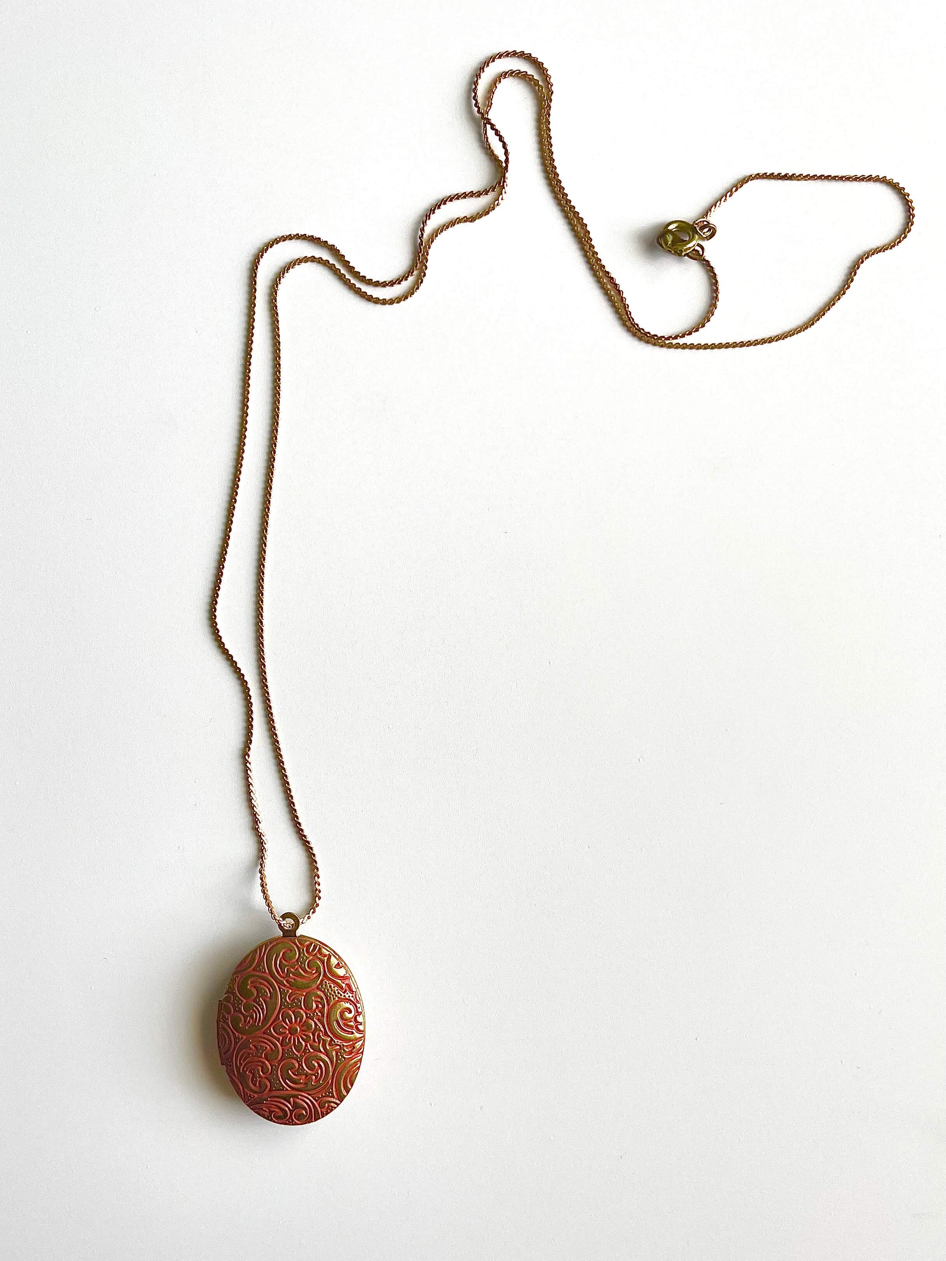 Yellow brass locket necklace with orange patina on a white background