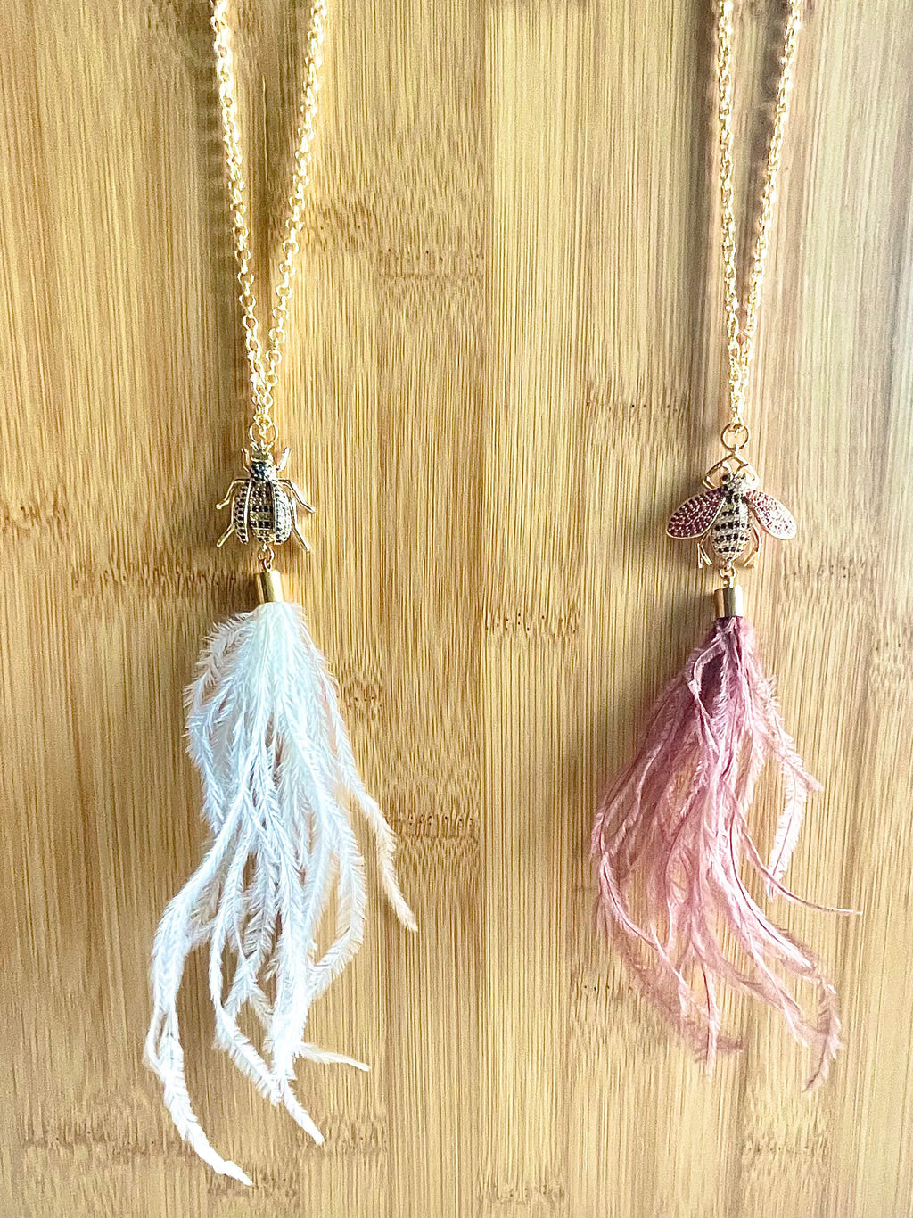 Ostrich feather and crystal bee pendant necklaces on wood background