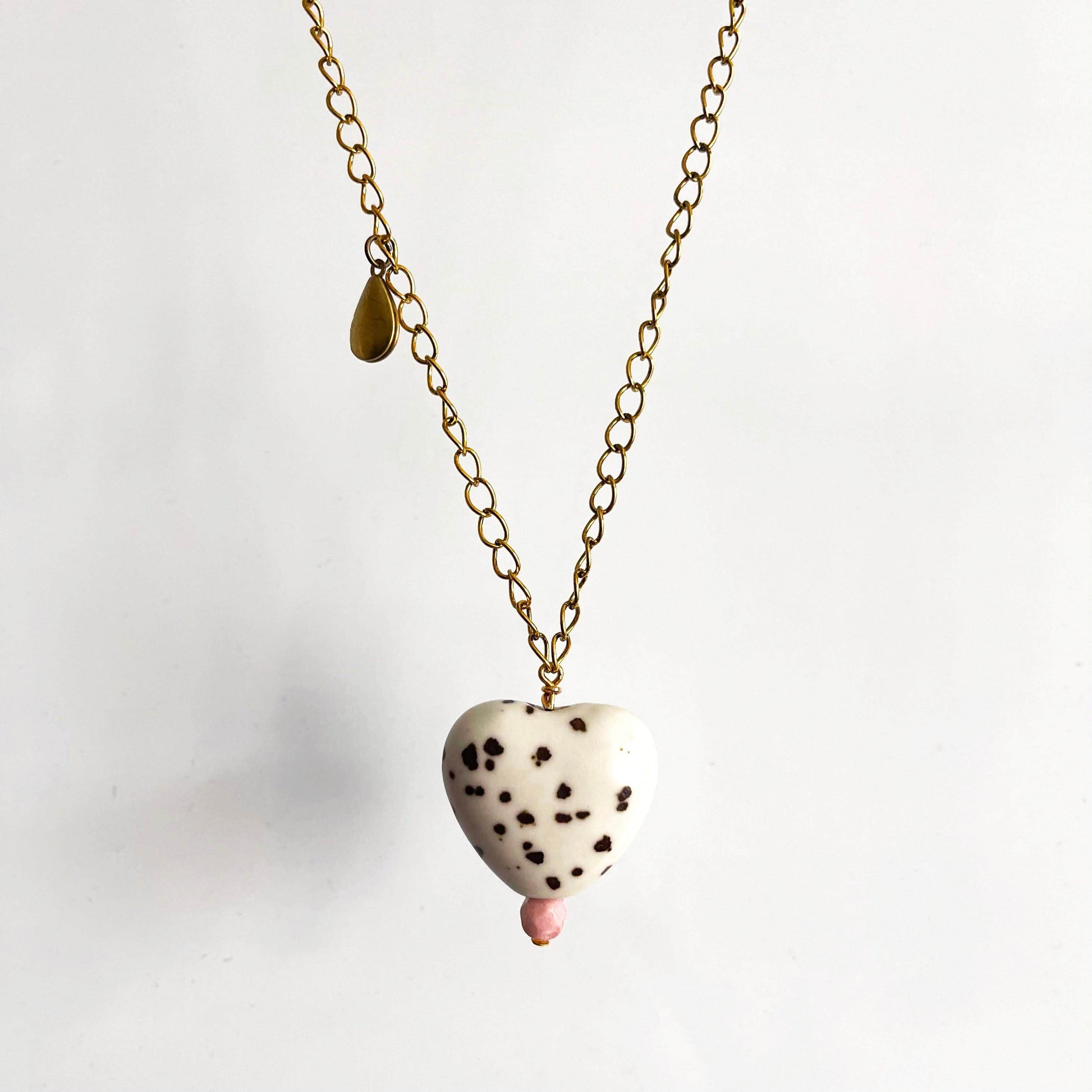 White ceramic heart pendant with brown spots and pink glass bead on a yellow brass chain with teardrop locket. 