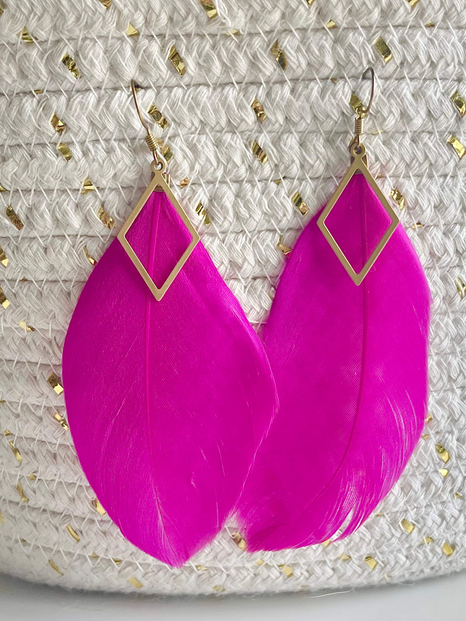 Pink feather earrings with gold accents on a textured surface