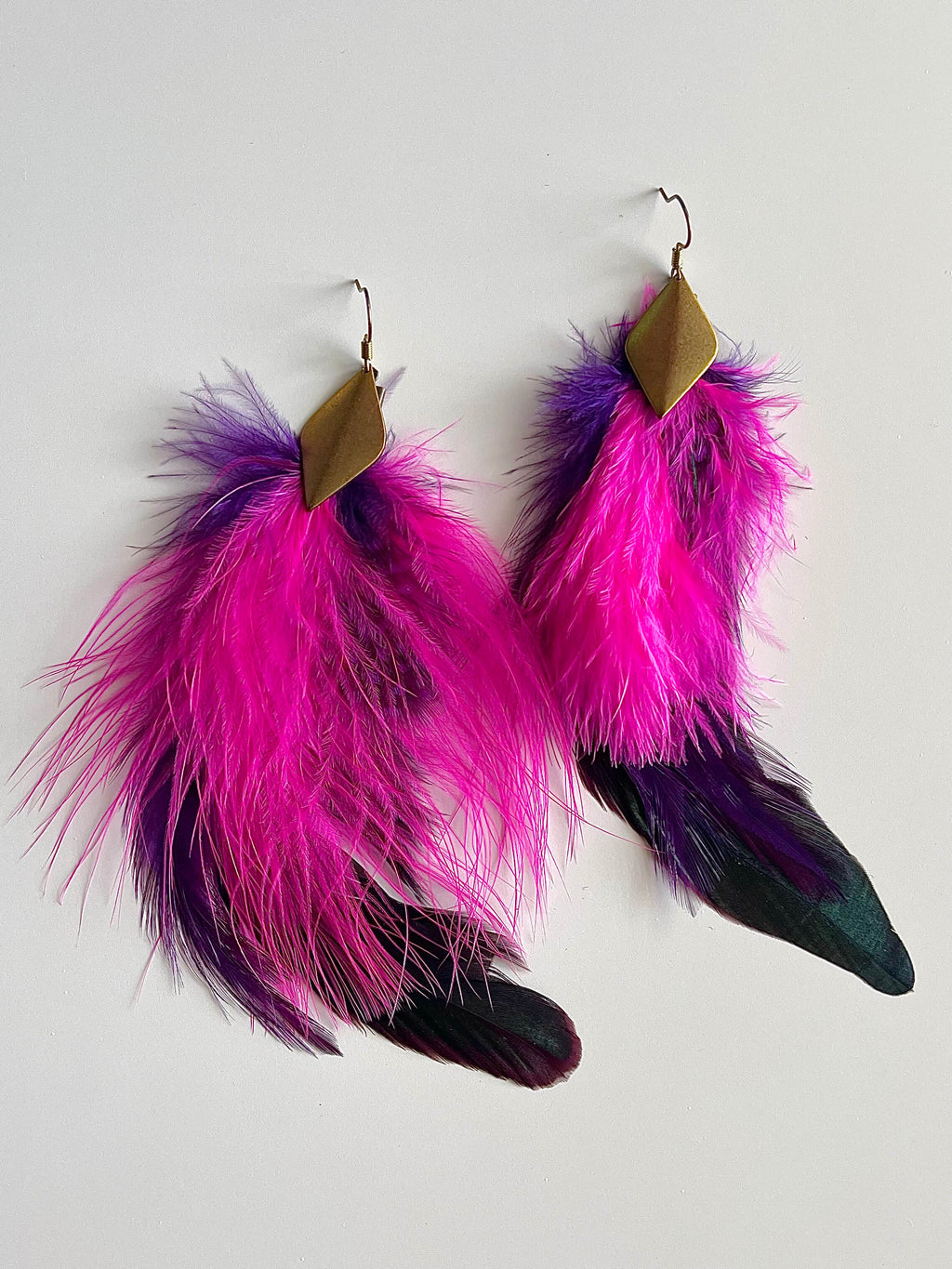 Pink and purple feather earrings with diamond shaped brass pendant on white background