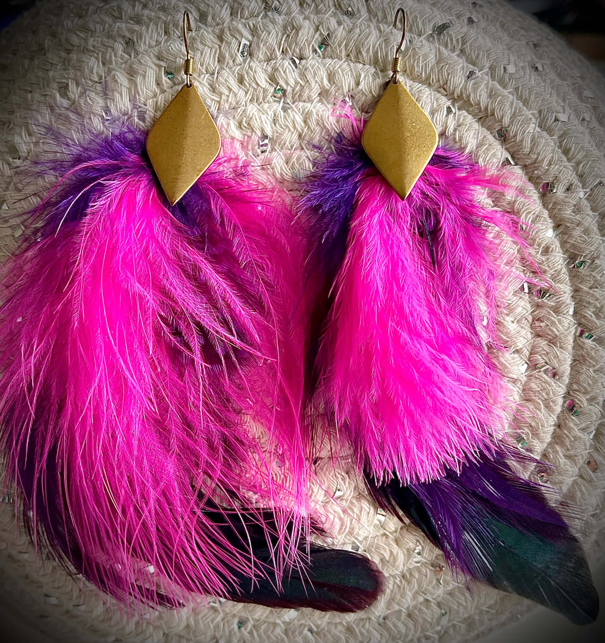 Pink and purple feather earrings with diamond shaped brass pendant on white background