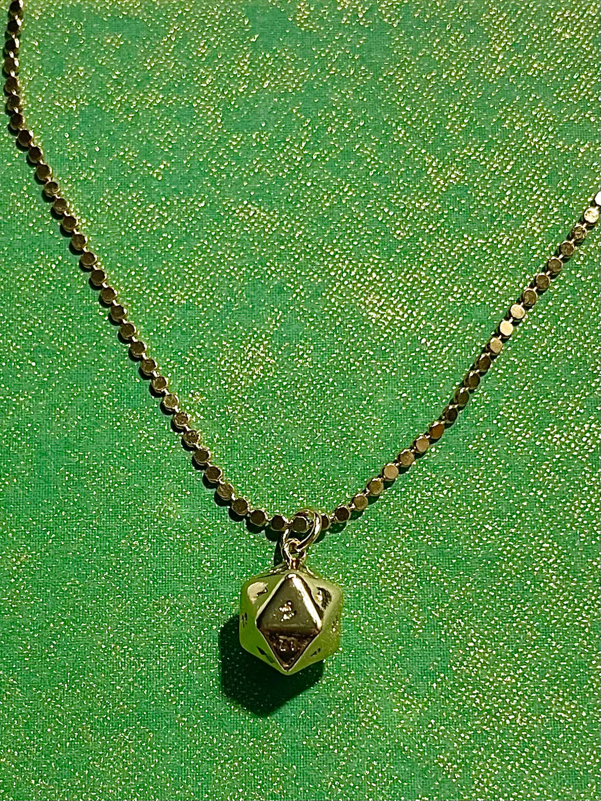 Yellow brass polyhedral charm on a dot chain with green background 
