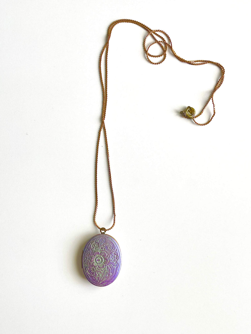 Yellow brass locket necklace with purple patina on a white background