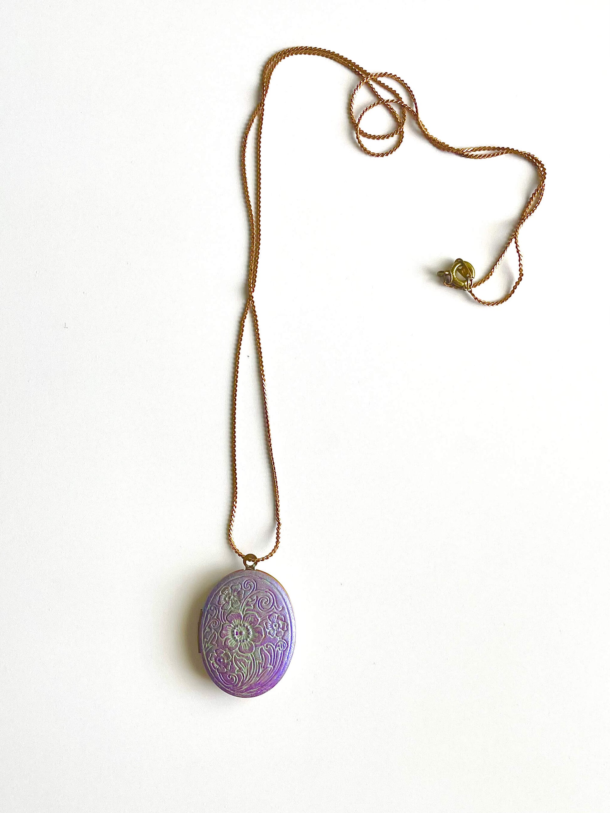 Yellow brass locket necklace with purple patina on a white background