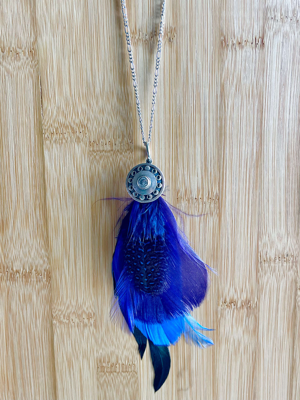 Blue and purple feathers with silver moon phase pendant on a silver chain with a wood backdrop
