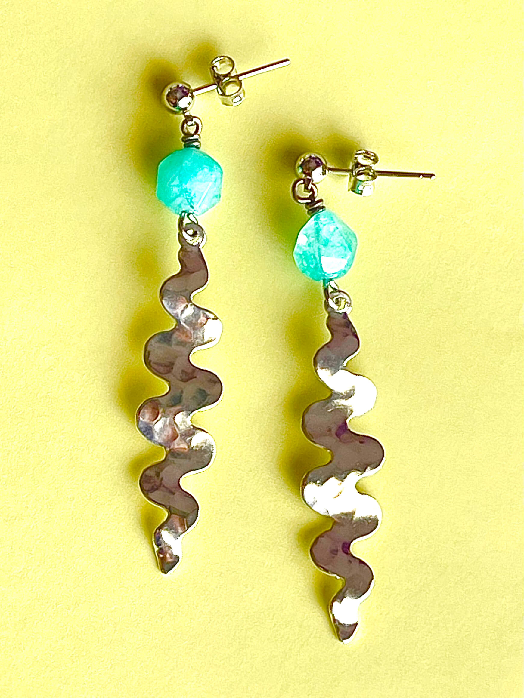 Stainless steel wavy pendant earrings with blue glass bead on a yellow background