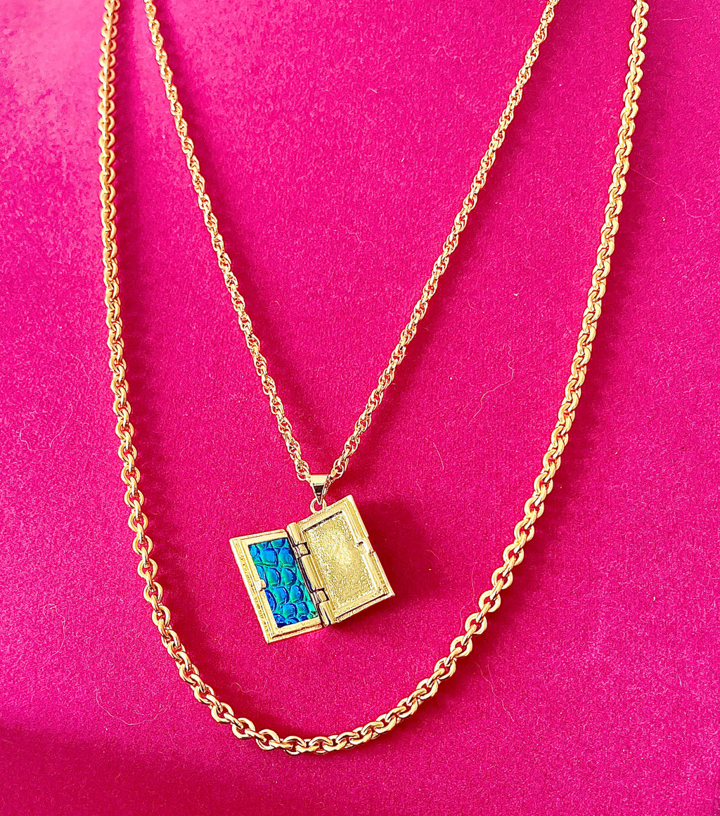 Yellow brass layered storybook locket necklace with two necklace chains on pink backdrop. 