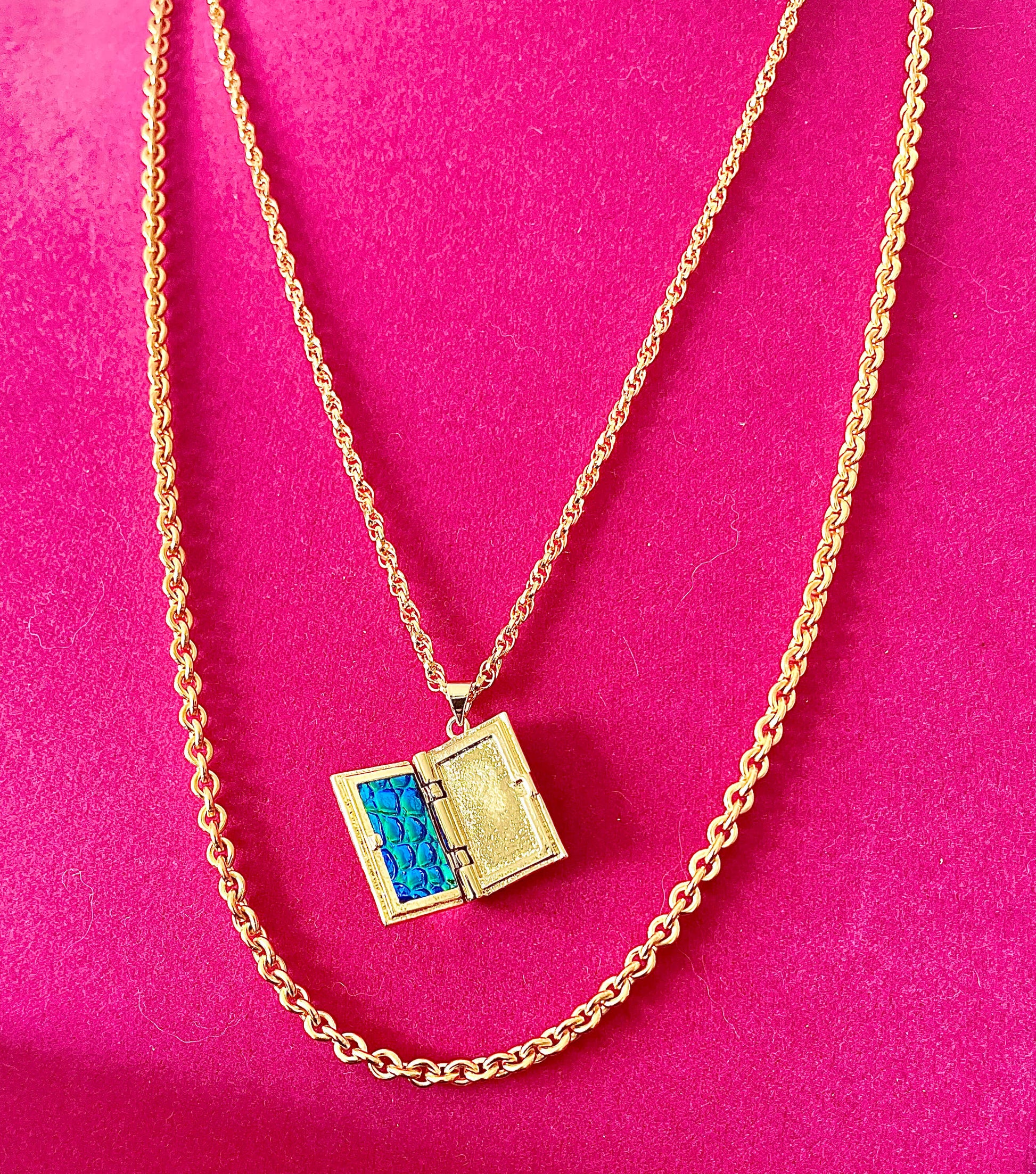 Yellow brass layered storybook locket necklace with two necklace chains on pink backdrop. 