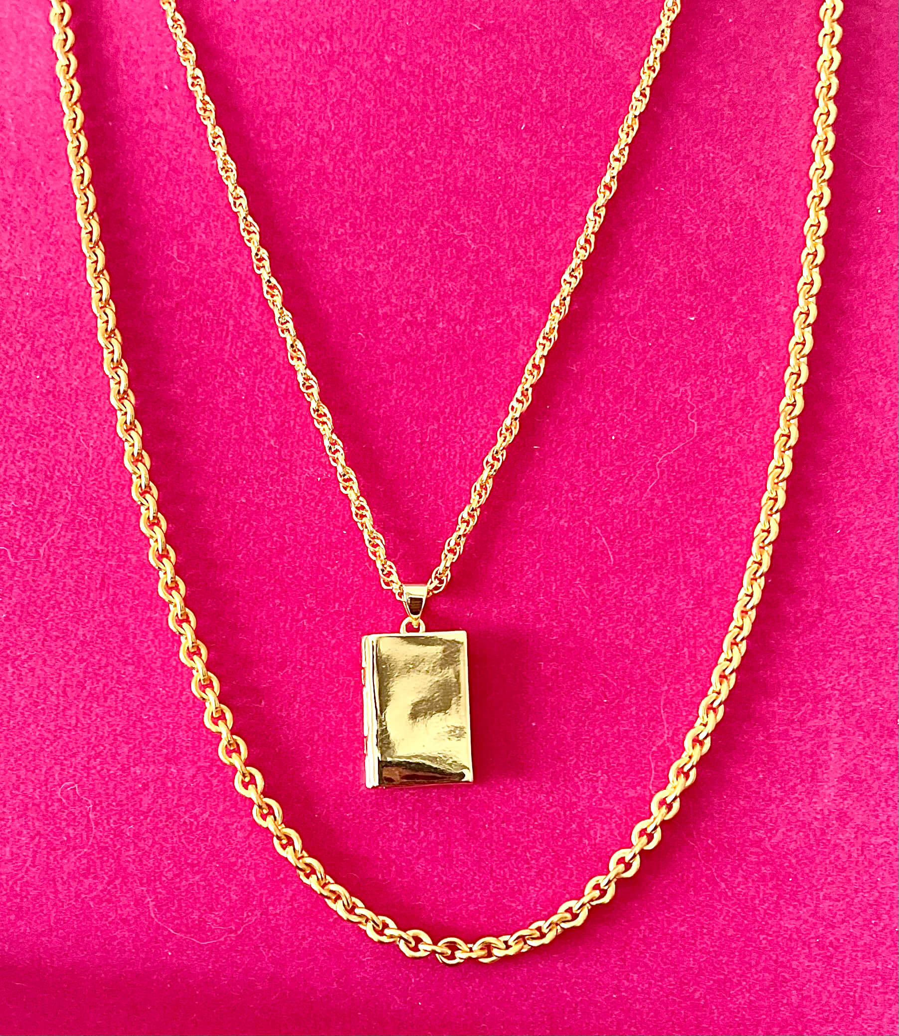 Yellow brass layered storybook locket necklace with two necklace chains on pink backdrop. 