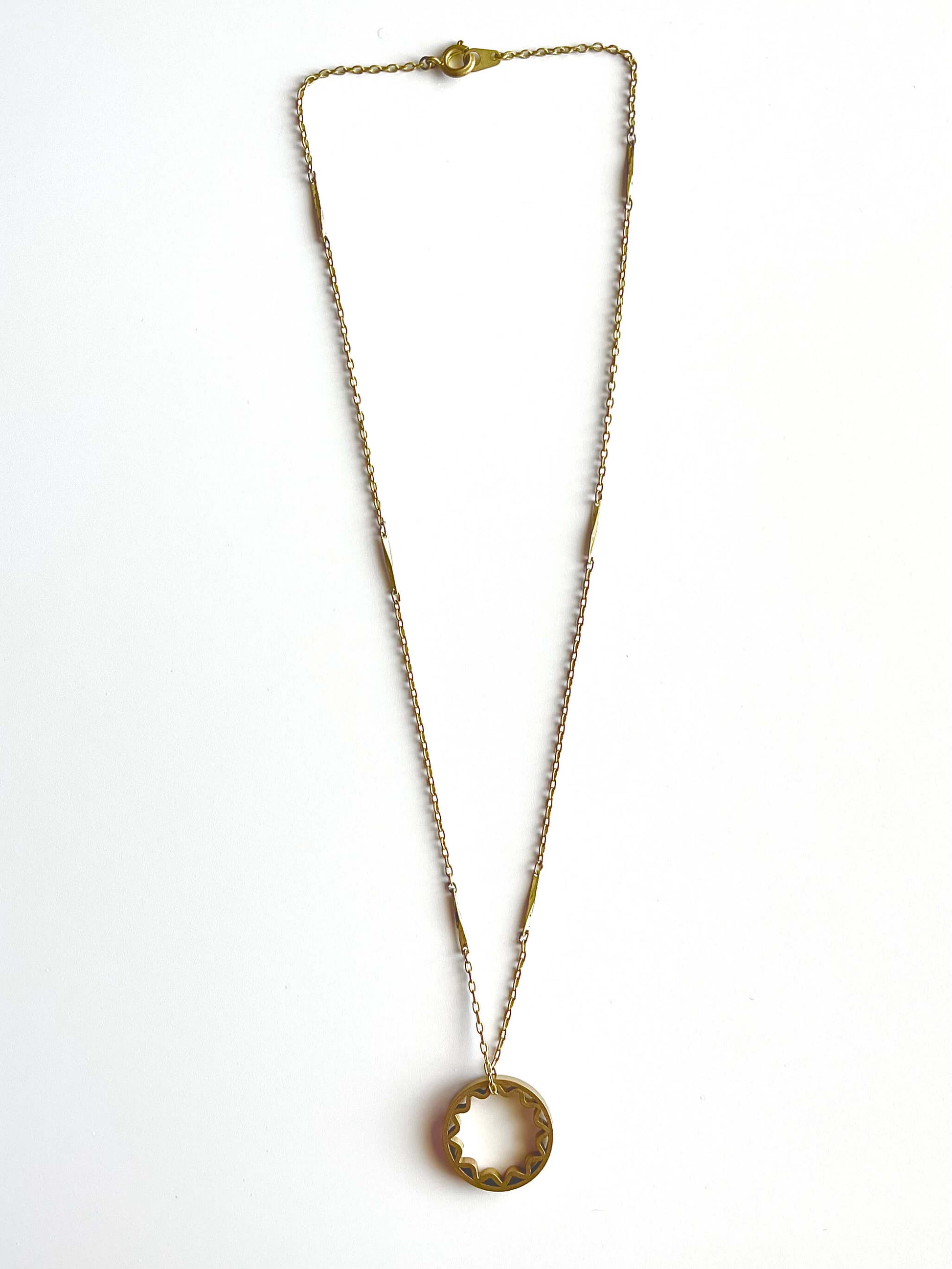 Yellow brass sun pendant on a yellow brass bar chain with a blue background