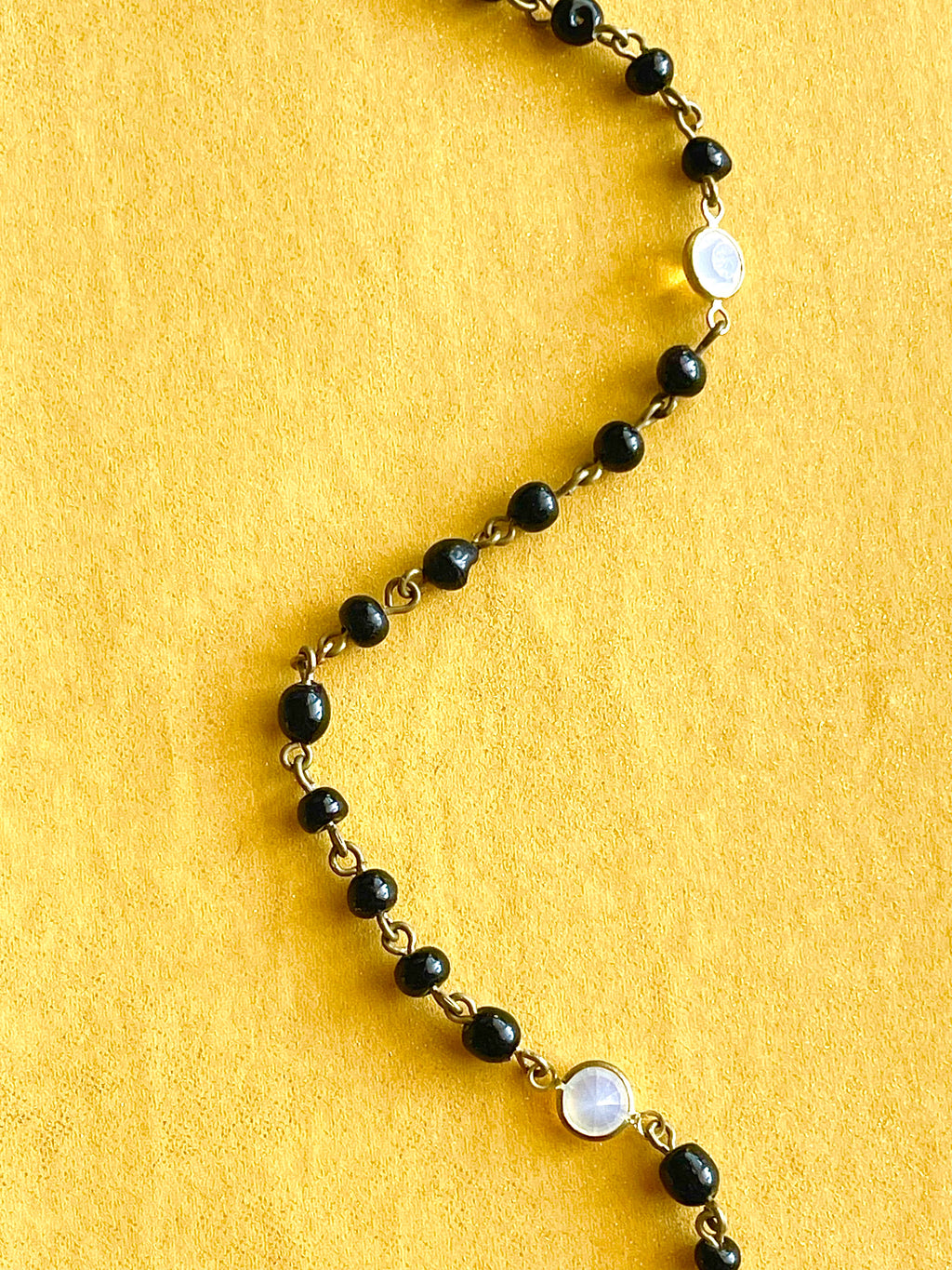 Black bead necklace with white crystal stations on a yellow background