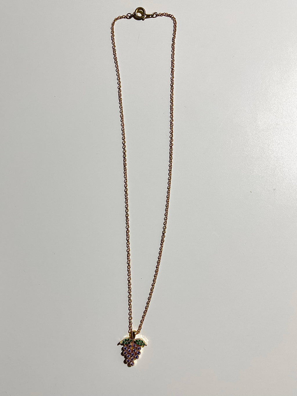 Yellow brass necklace with purple grape charm on white background 
