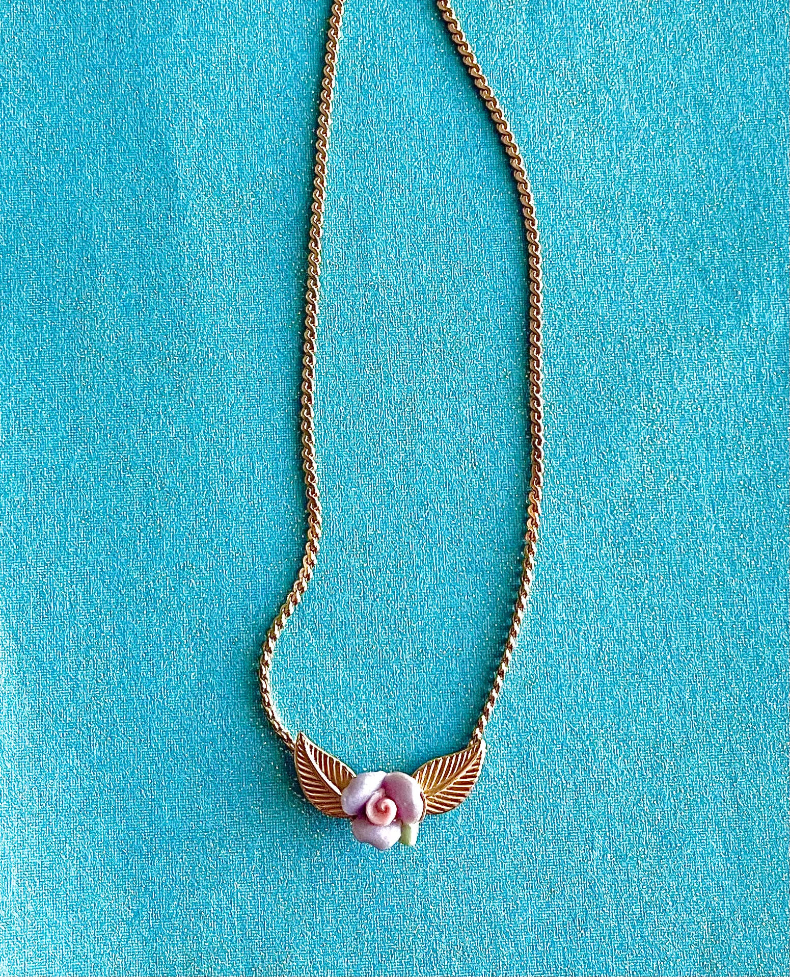 Yellow brass necklace with purple and pink clay flower on a blue background