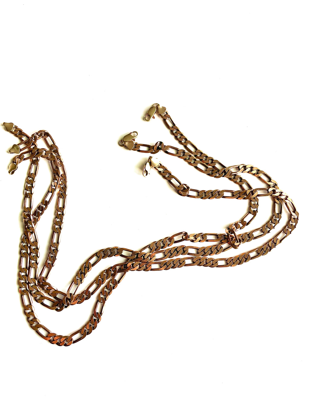 Three brass Figaro chain necklaces laying organically against a white backdrop. 