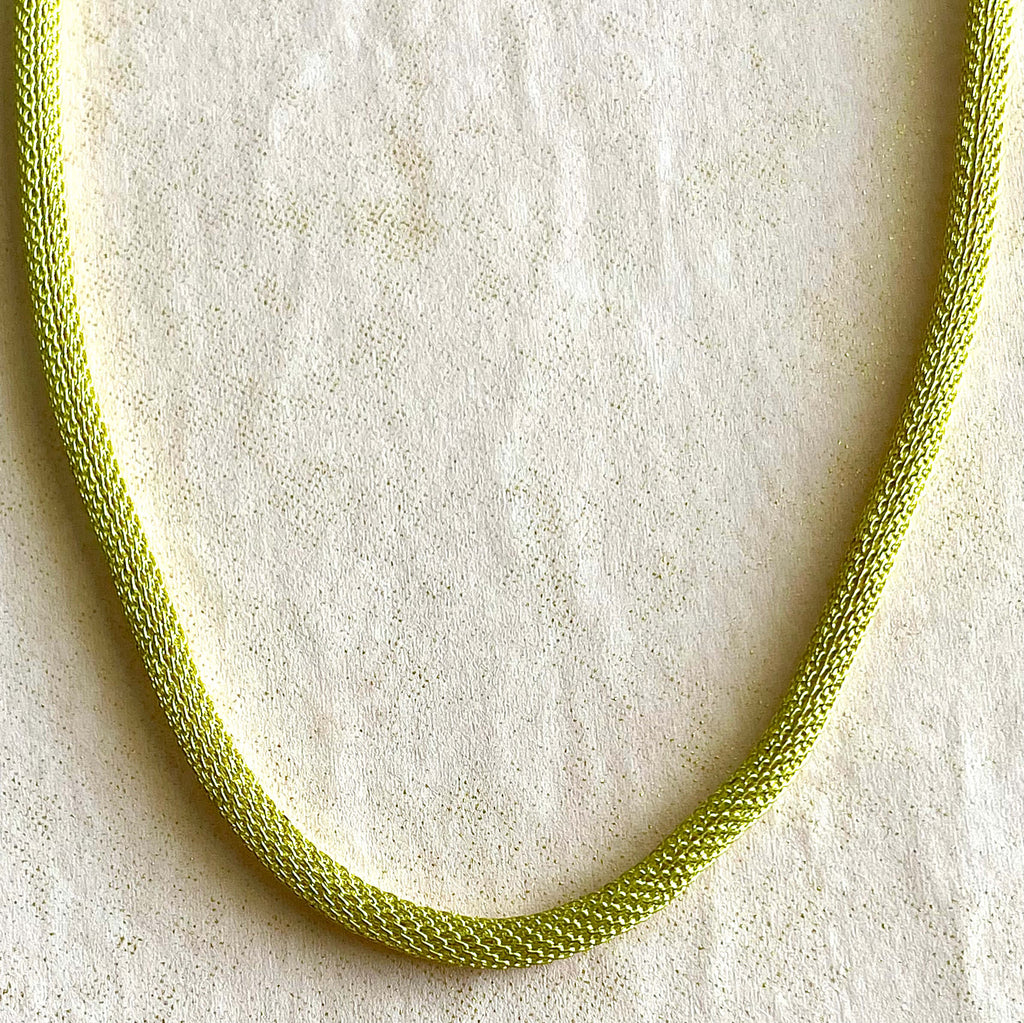 Yellow brass mesh necklace on pink background