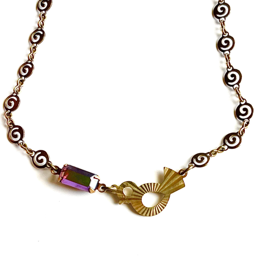 Yellow brass swirl link chain with patterned bird charm and fuchsia crystal bracelet set against white backdrop. 