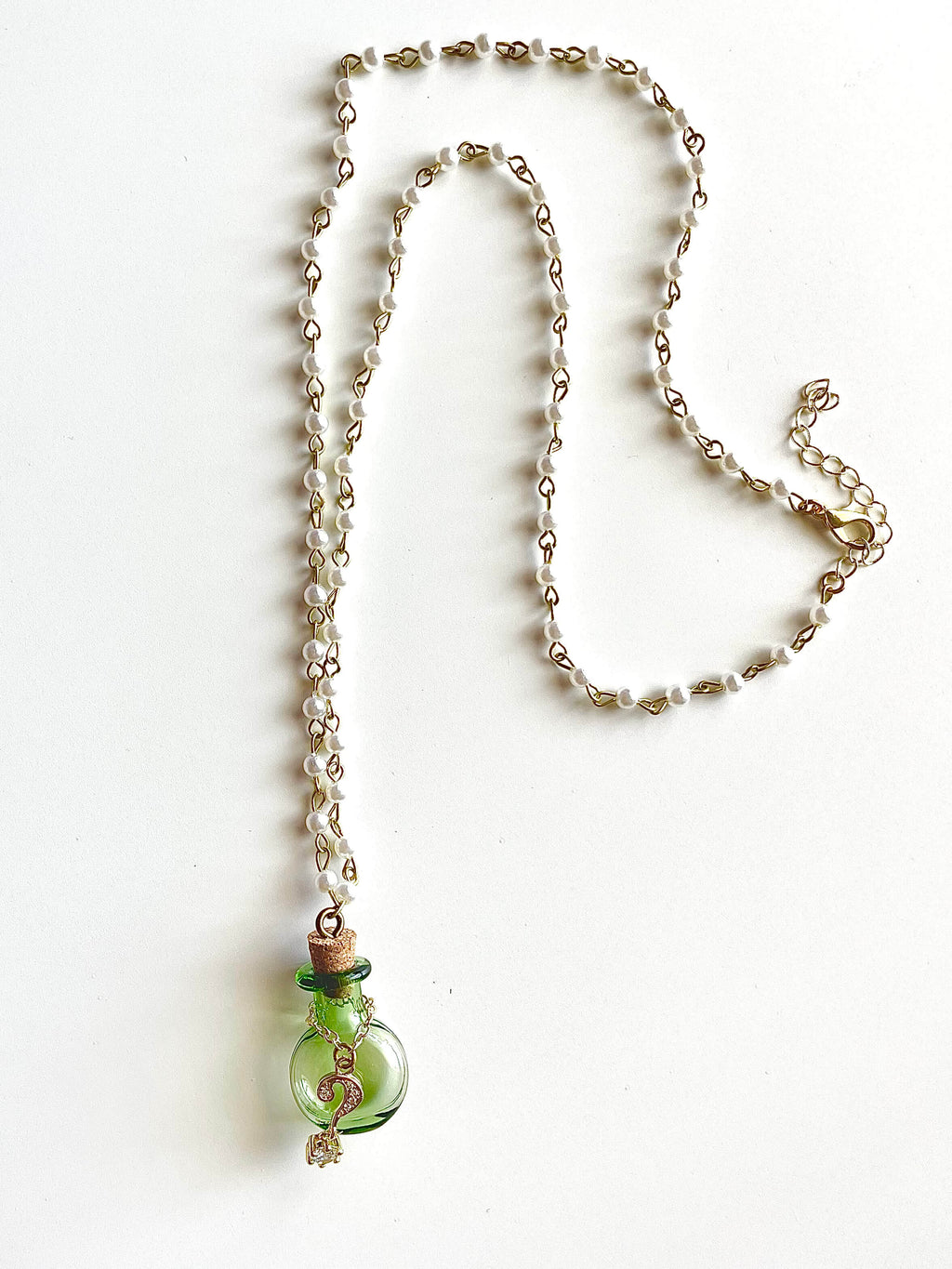 White faux pearl chain with green bottle and gold question mark pendant necklace on white background