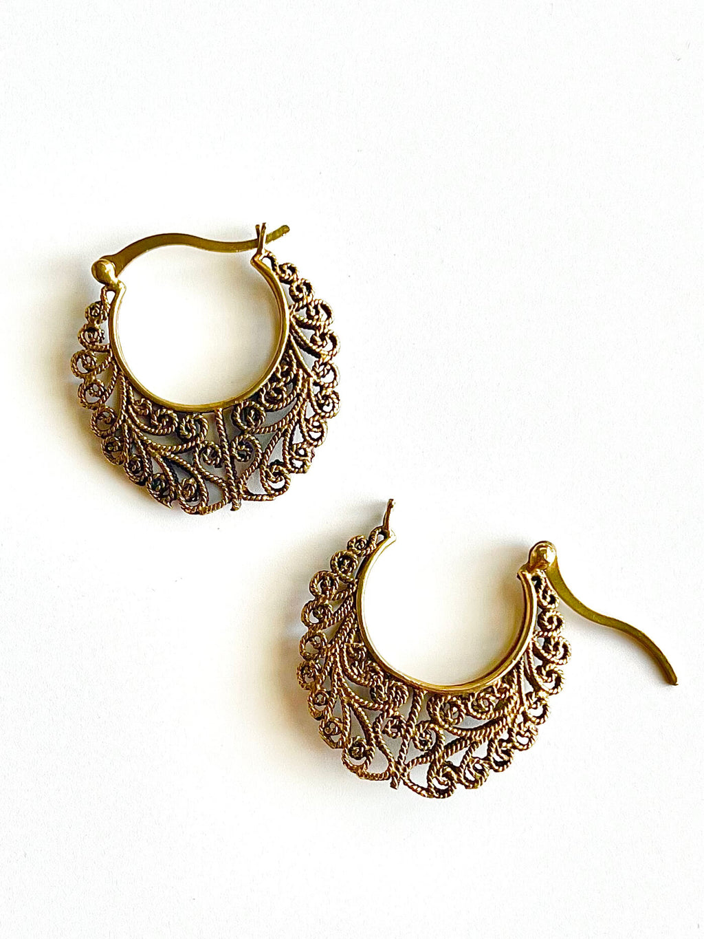 Pair of brass filigree hoop earrings on a white background
