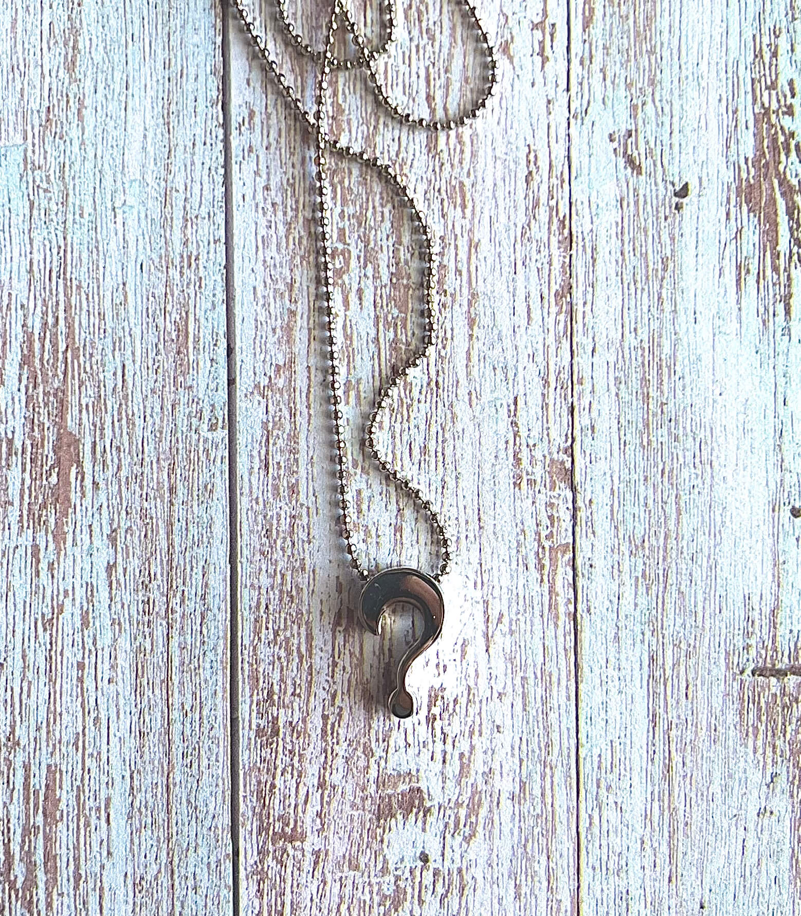 Necklace with a question mark pendant on a wooden surface