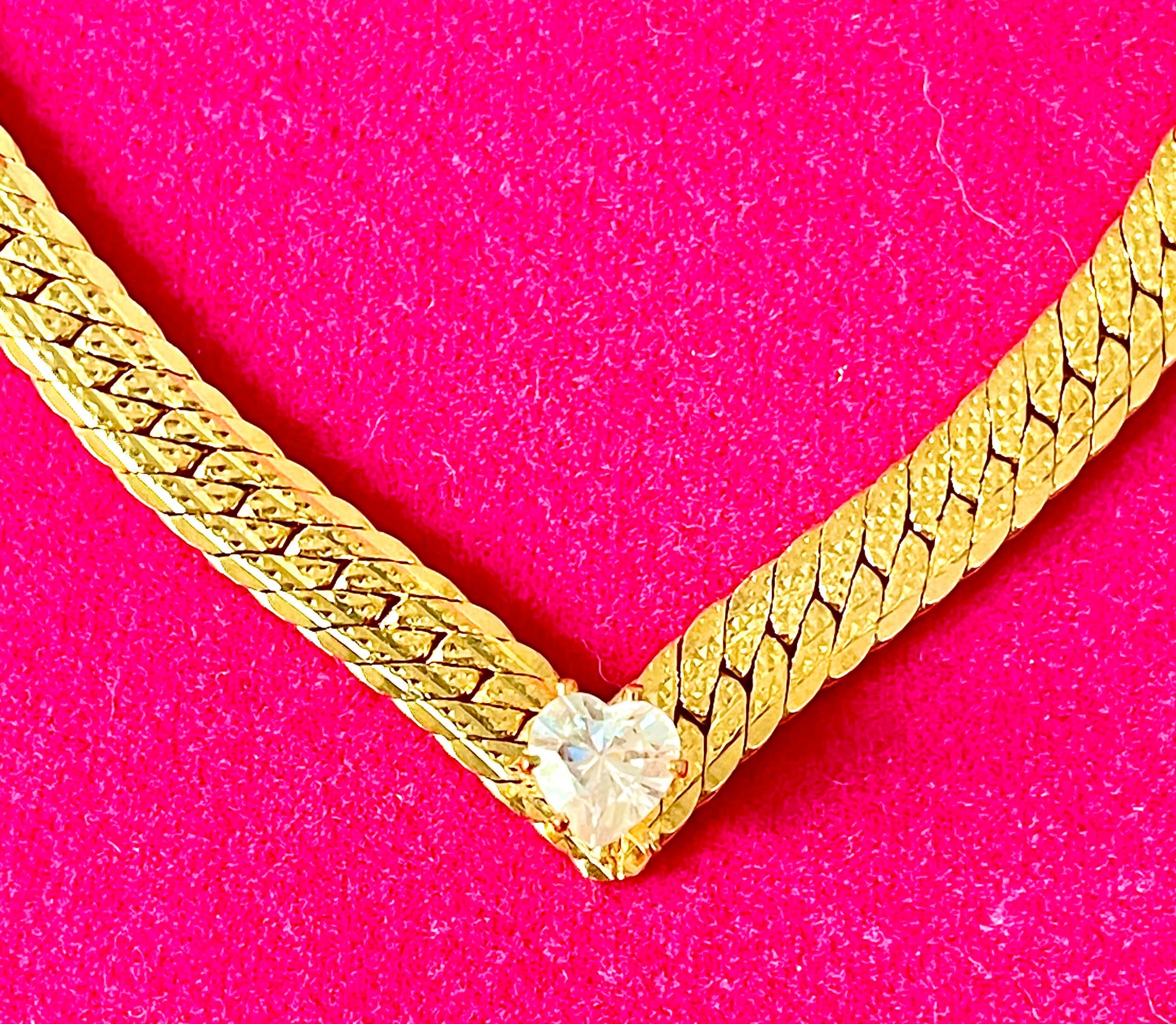 Yellow brass flat curb necklace with heart shaped crystal on pink background