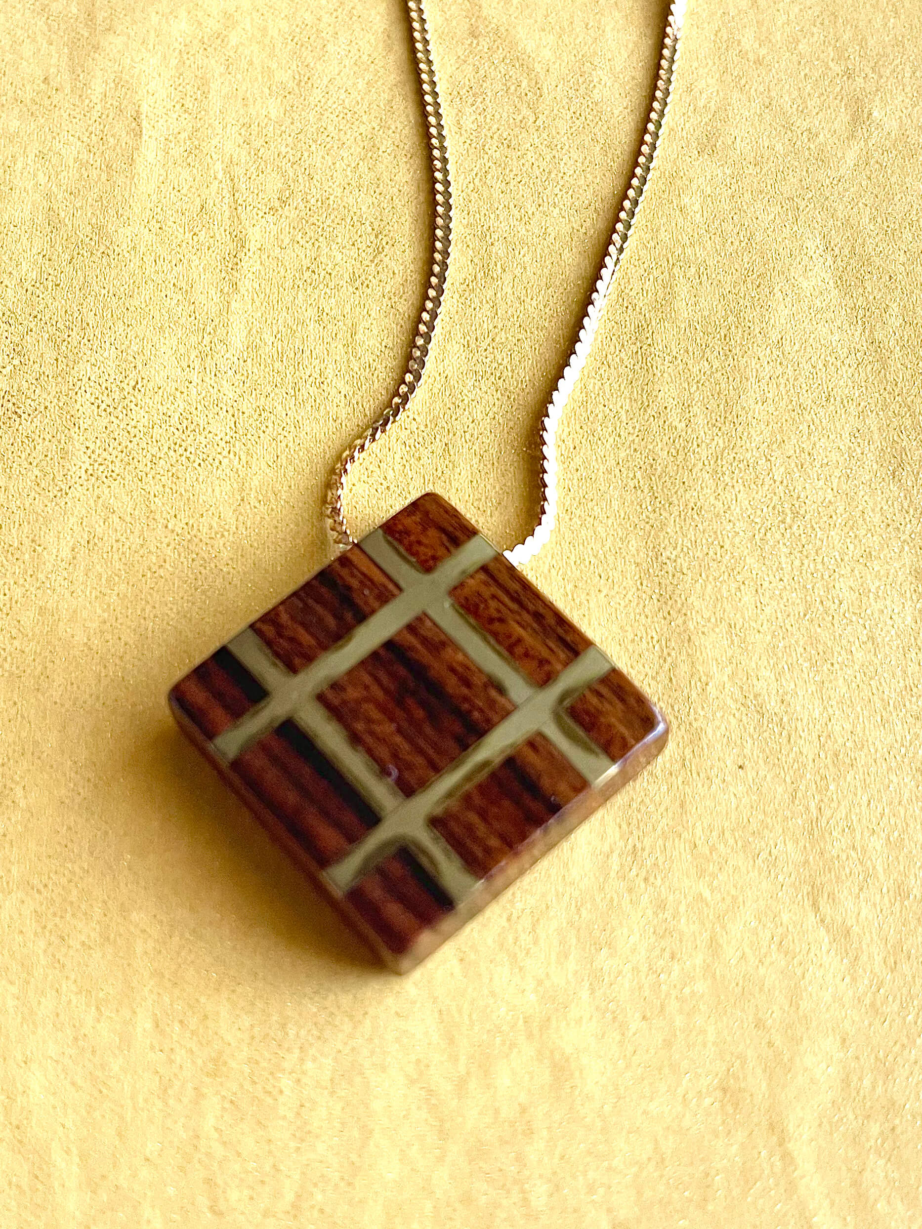 Square wood pendant with yellow brass grid inlay on yellow brass chain with yellow background