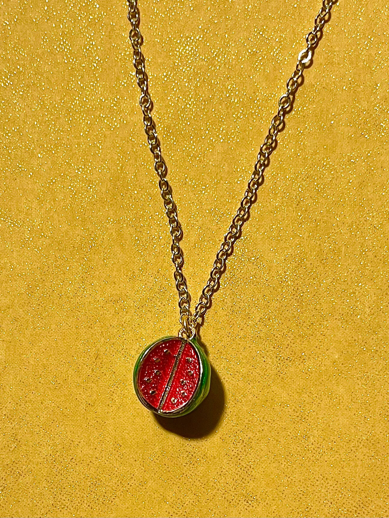 Watermelon charm on a gold chain with yellow background