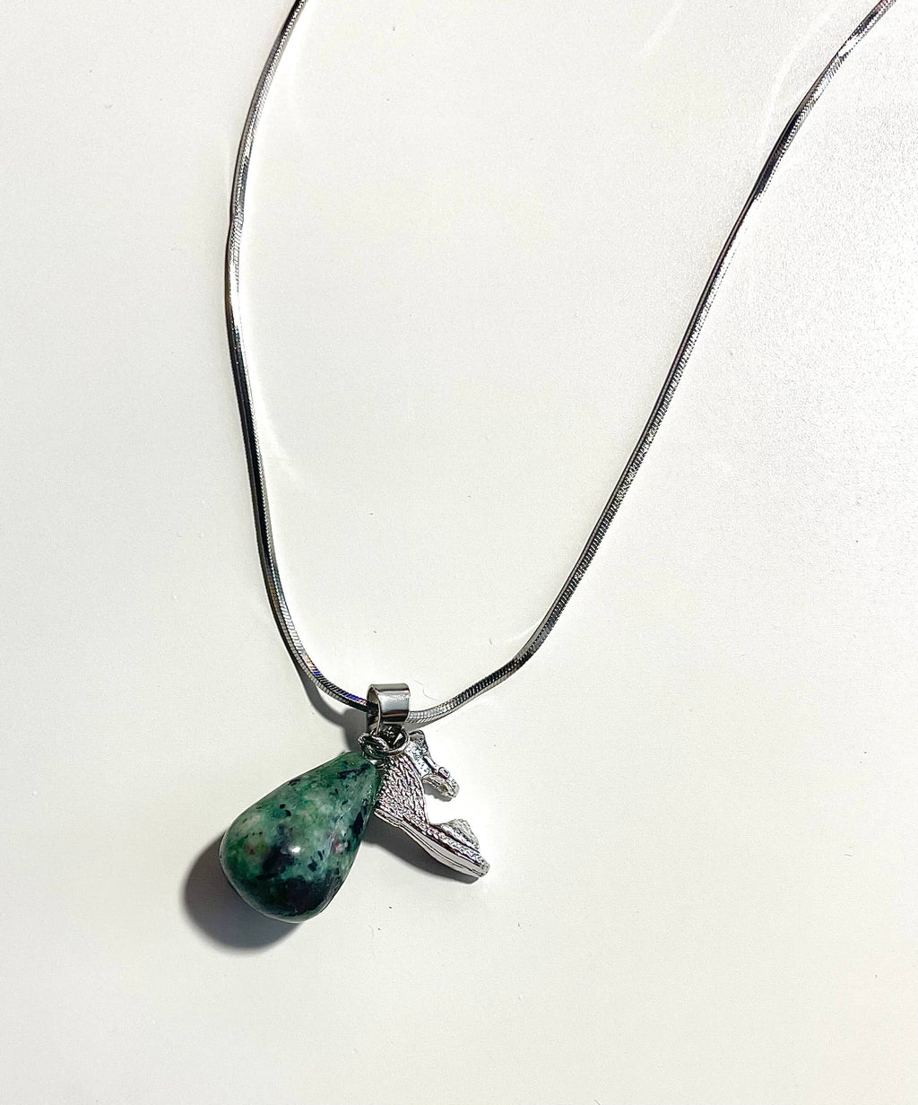 Silver necklace with green and black gemstone and shoe charm on a white backdrop
