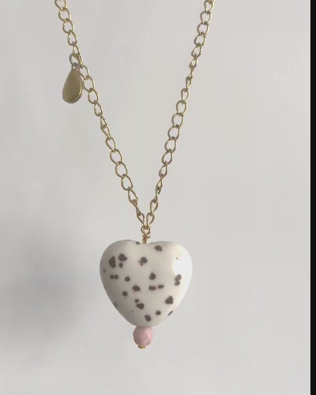 White ceramic heart pendant with brown spots and yellow brass teardrop locket on a yellow brass chain. 