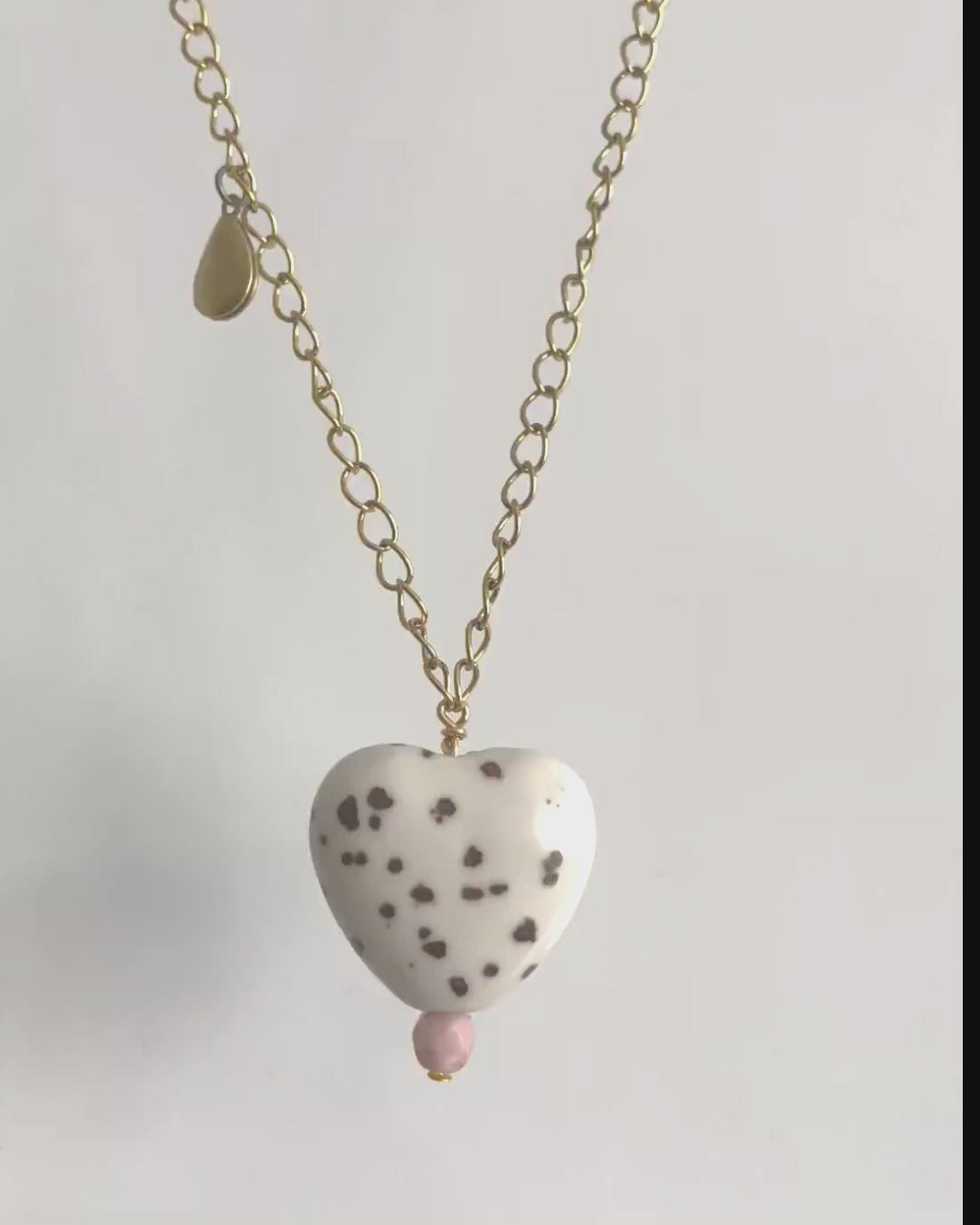 White ceramic heart pendant with brown spots and yellow brass teardrop locket on a yellow brass chain. 